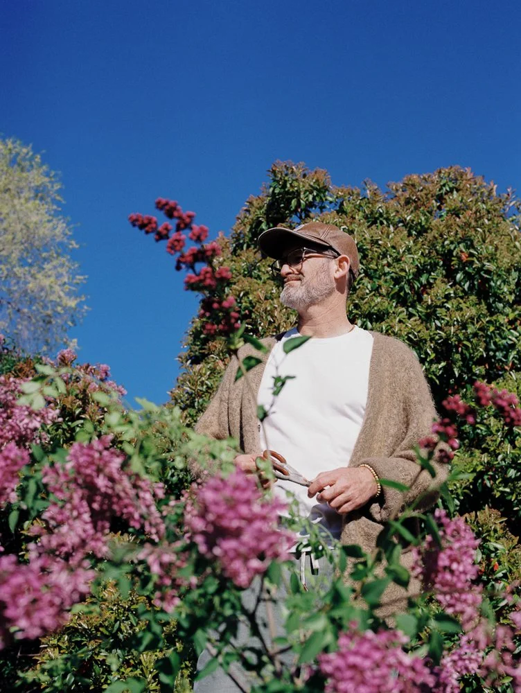 film portrait of man in cardigan, hat, glasses against lilac bush and blue sky
