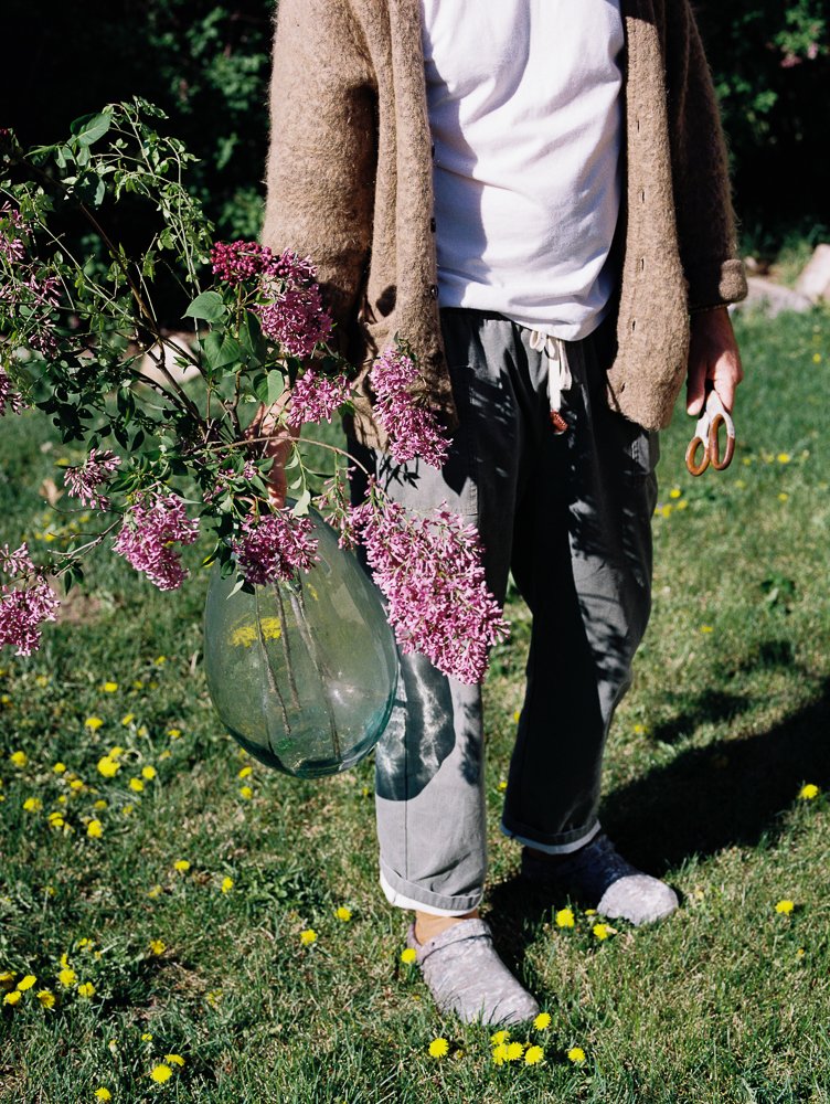 man holds large glass vase with lilacs