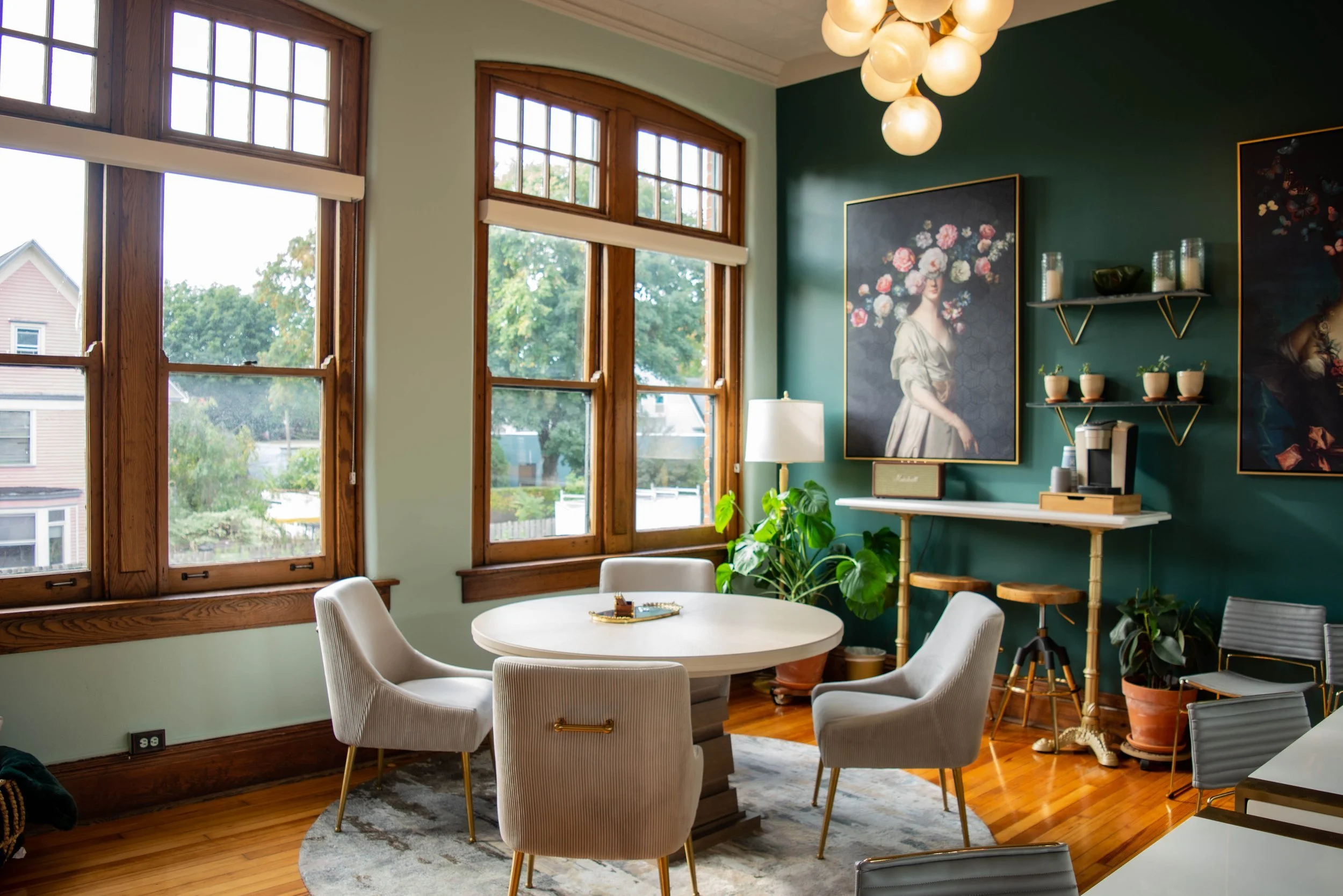 Stylish lounge room at The Historic German House featuring large windows, velvet chairs around a round table, green walls with floral art, and a cozy coffee station.