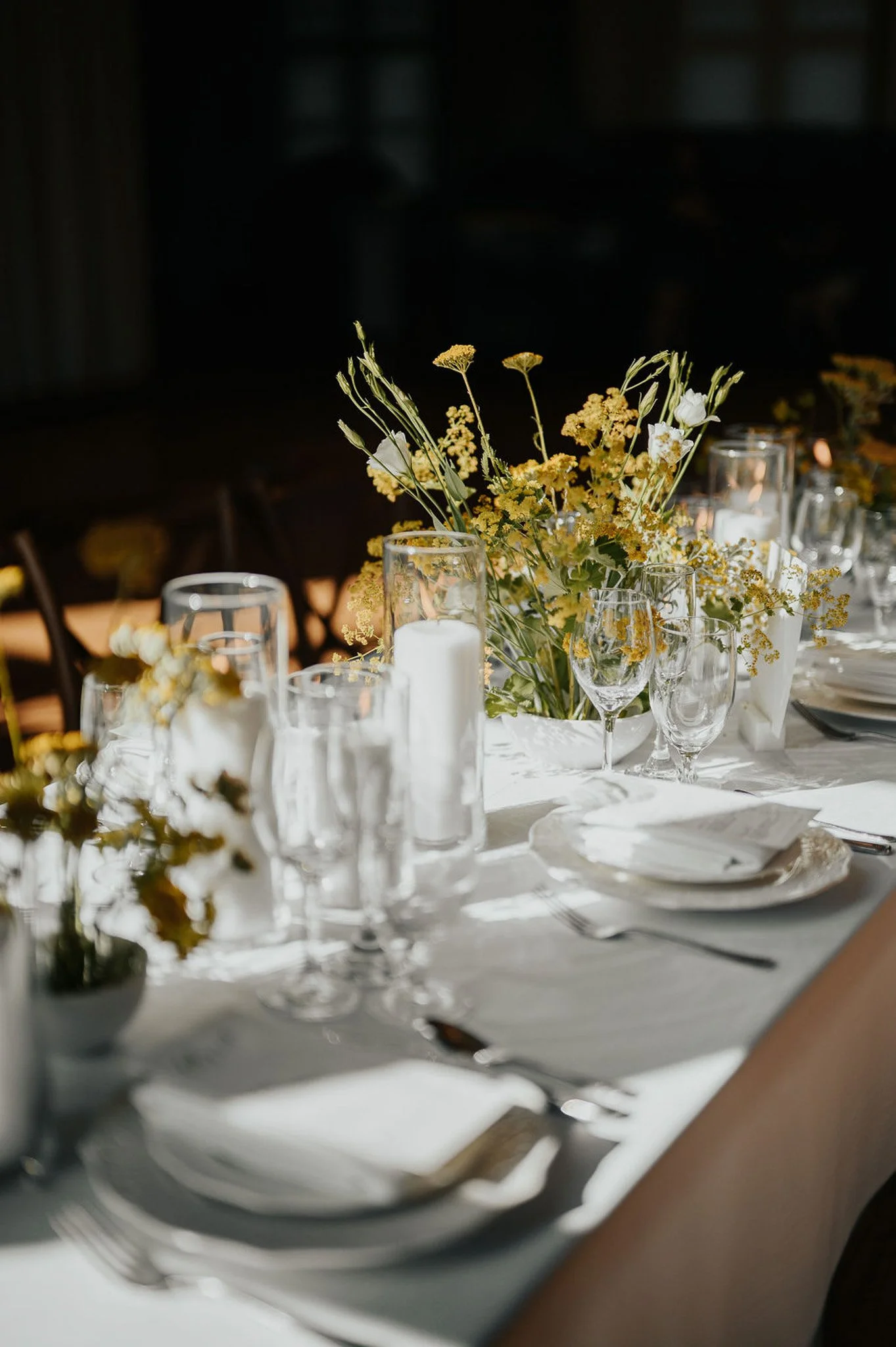 Elegant spring wedding table setting with pressed white linens, glass pillar candles, and yellow wildflower centerpieces at The Historic German House.