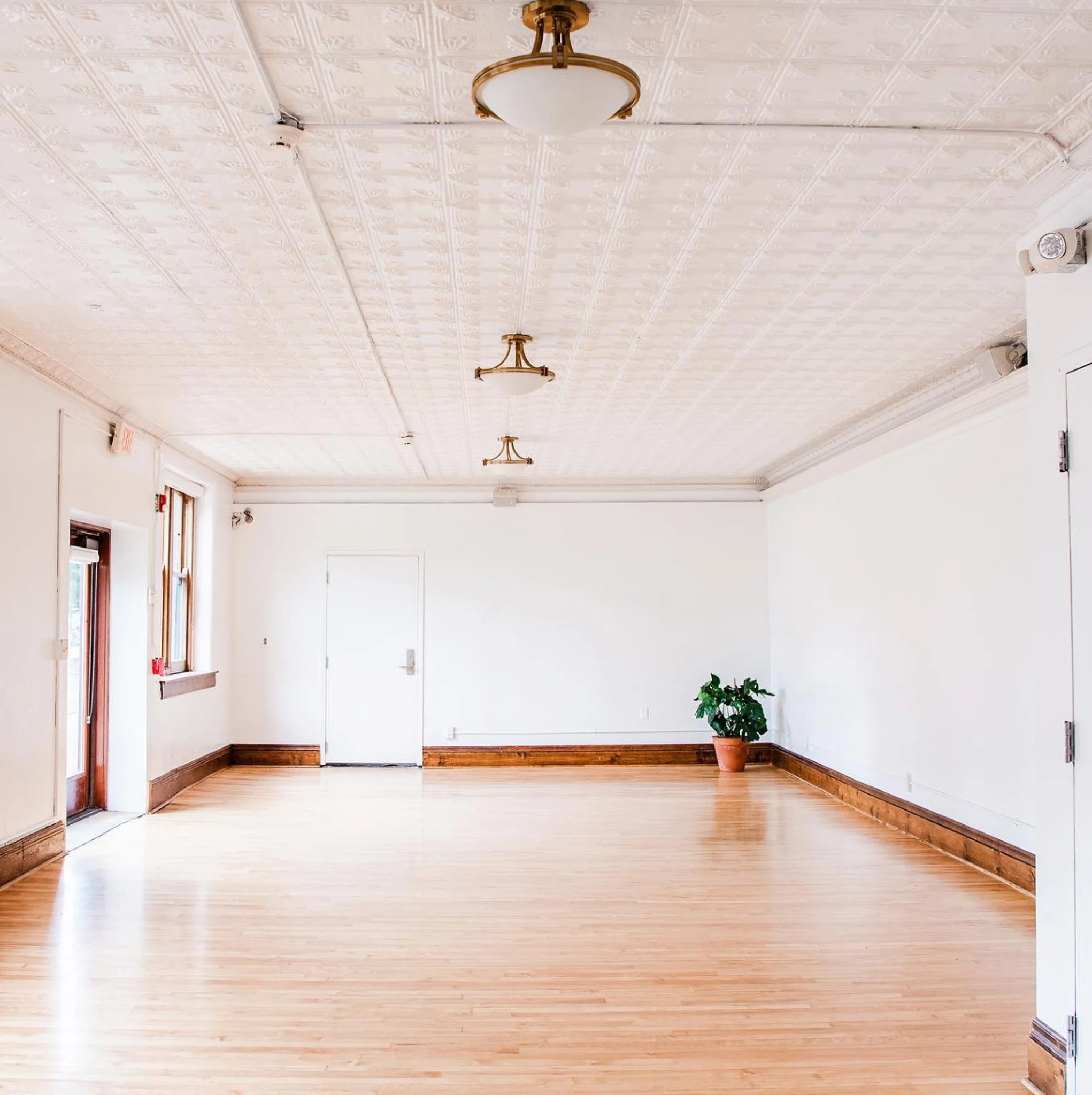 The Nicholson Room at The Historic German House, shown empty with hardwood floors, tin ceiling, and bright natural light pouring through windows.