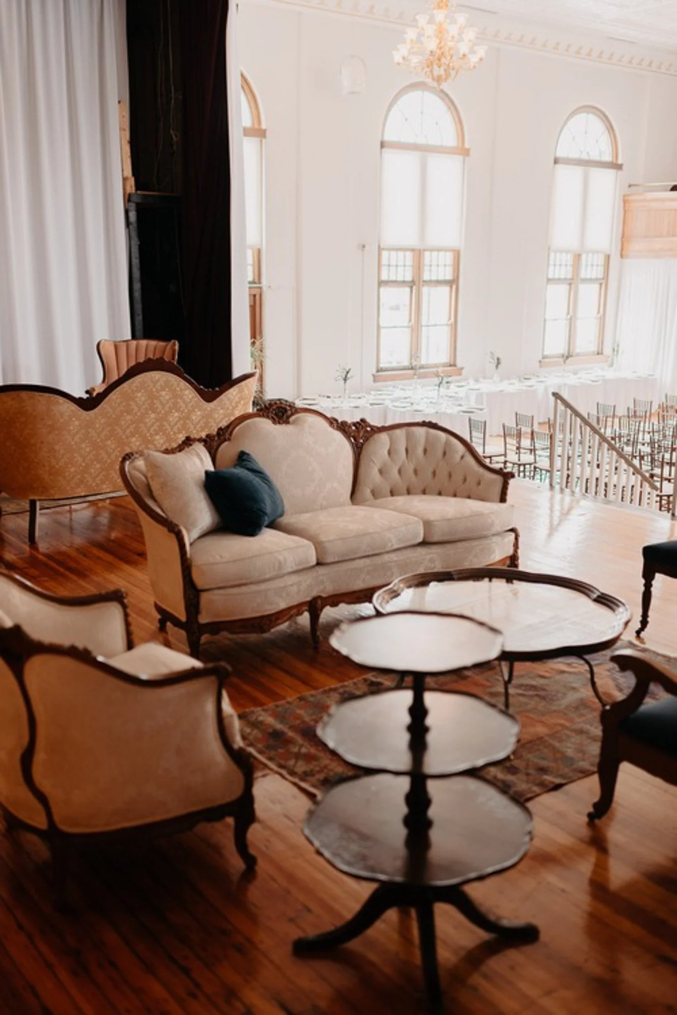 Vintage ivory and blush tufted sofas arranged in an upper lounge area at The Historic German House, overlooking sunlit reception tables and arched windows.