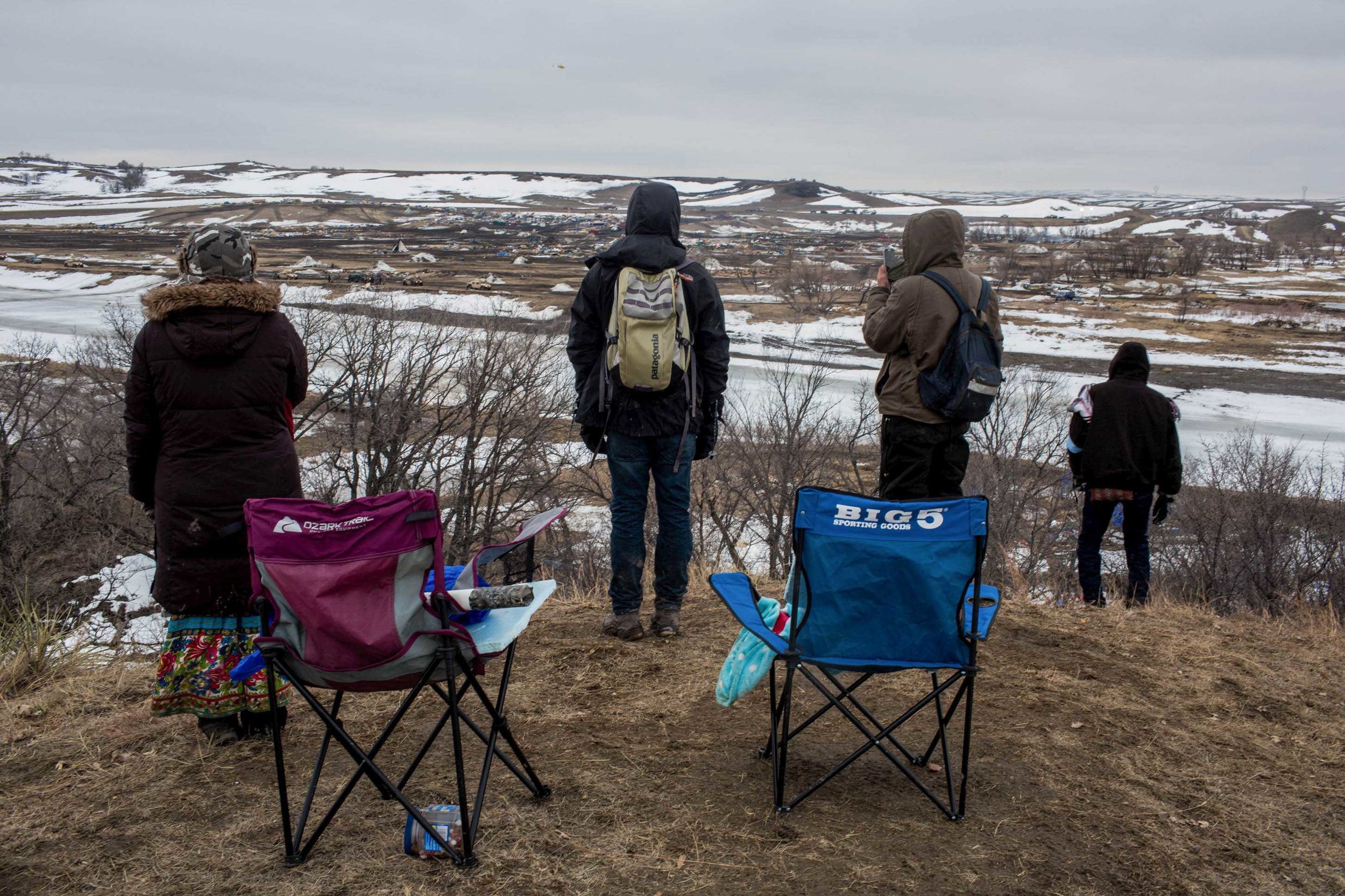  Water Protectors stand on the hill overlooking Oceti Sakowin, watching highly militarized BIA, ATF and Morton County Sheriffs bulldoze the remains of the camp several hours after the raid on Wednesday morning. Wednesday February 23rd 2017, Sacred St