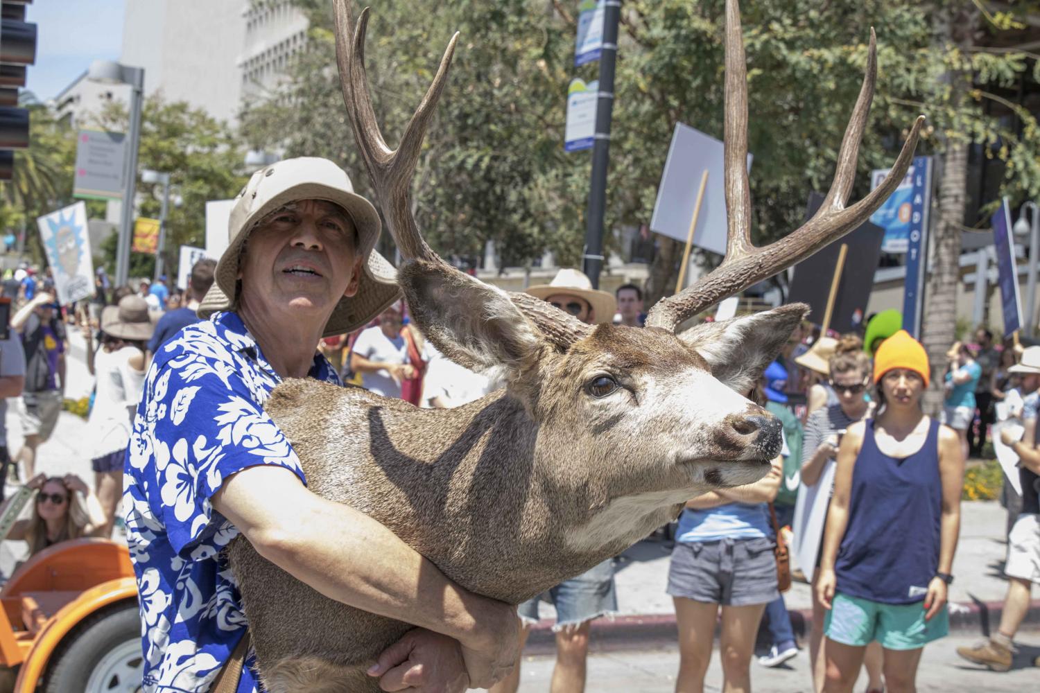  Mike Gloria, a protestor at the Earth Day March in Downtown Los Angeles, California on April 22, 2017 watches a choir presentation a he holds a deer head to show that when the earth goes, us and all the animals go with it. Zane Meyer-Thornton. 