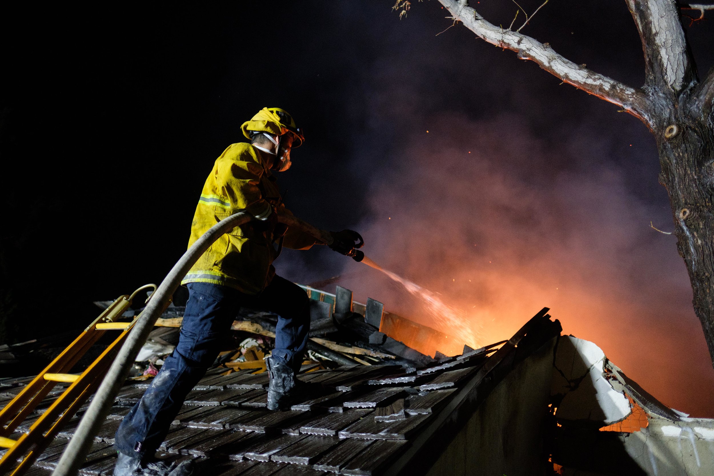     Los Angeles Fire Department firefighter on a rooftop, hosing down a flame inside the house. The LAFD has been battling the Skirball Fire since the early morning of Dec. 6, 2017. In Los Angeles, Calif. (Photo by Jayrol San Jose) 