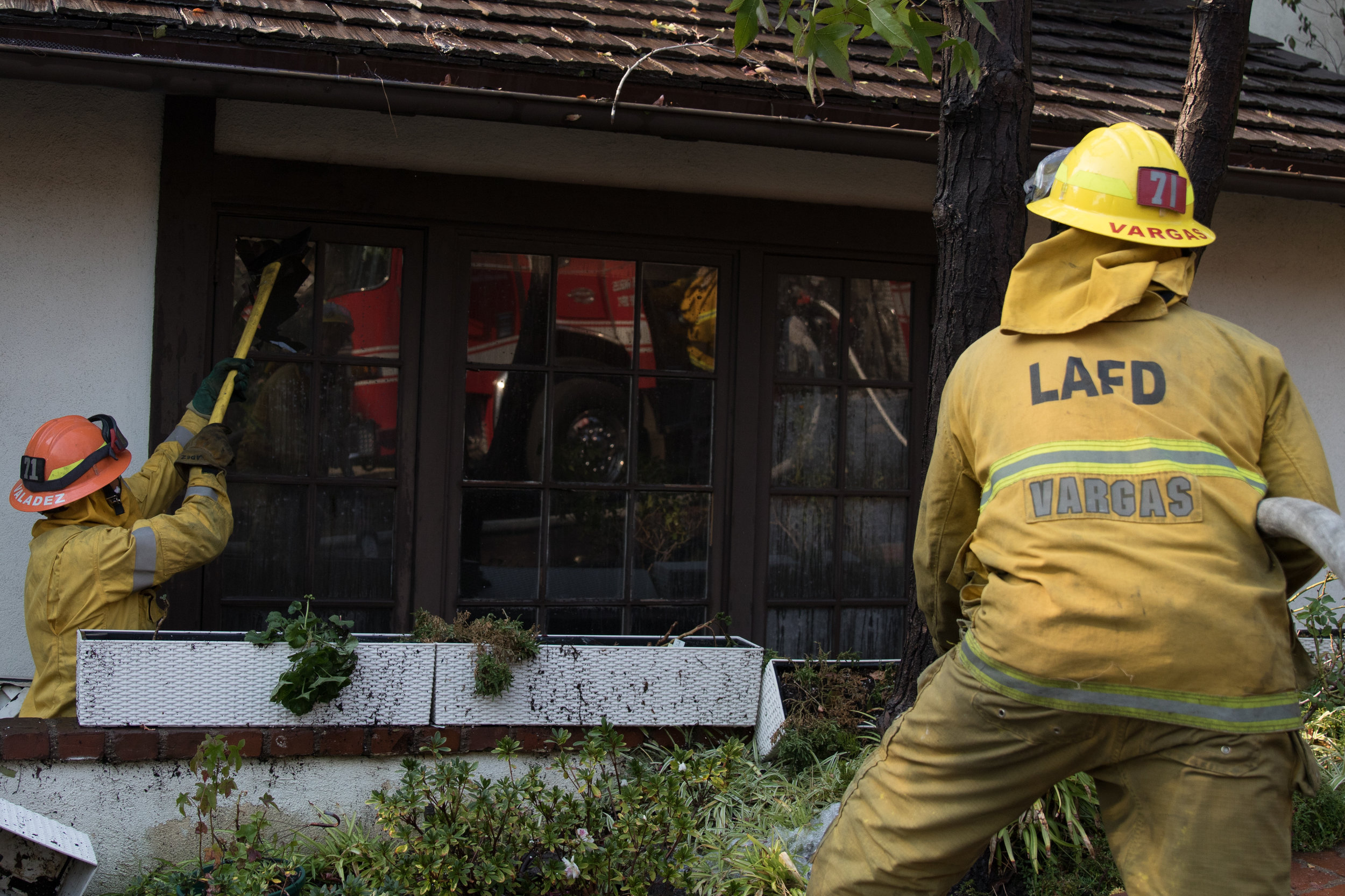  Luis Vargas (right) prepares to fire his hose as David Valadez (left) breaks down a window of one of the burning houses in the Skirball Fire. The fire burned 450 acres and shut down the 405 freeway on Dec.&nbsp;6, 2017 in West Los Angeles Calif. (Ph