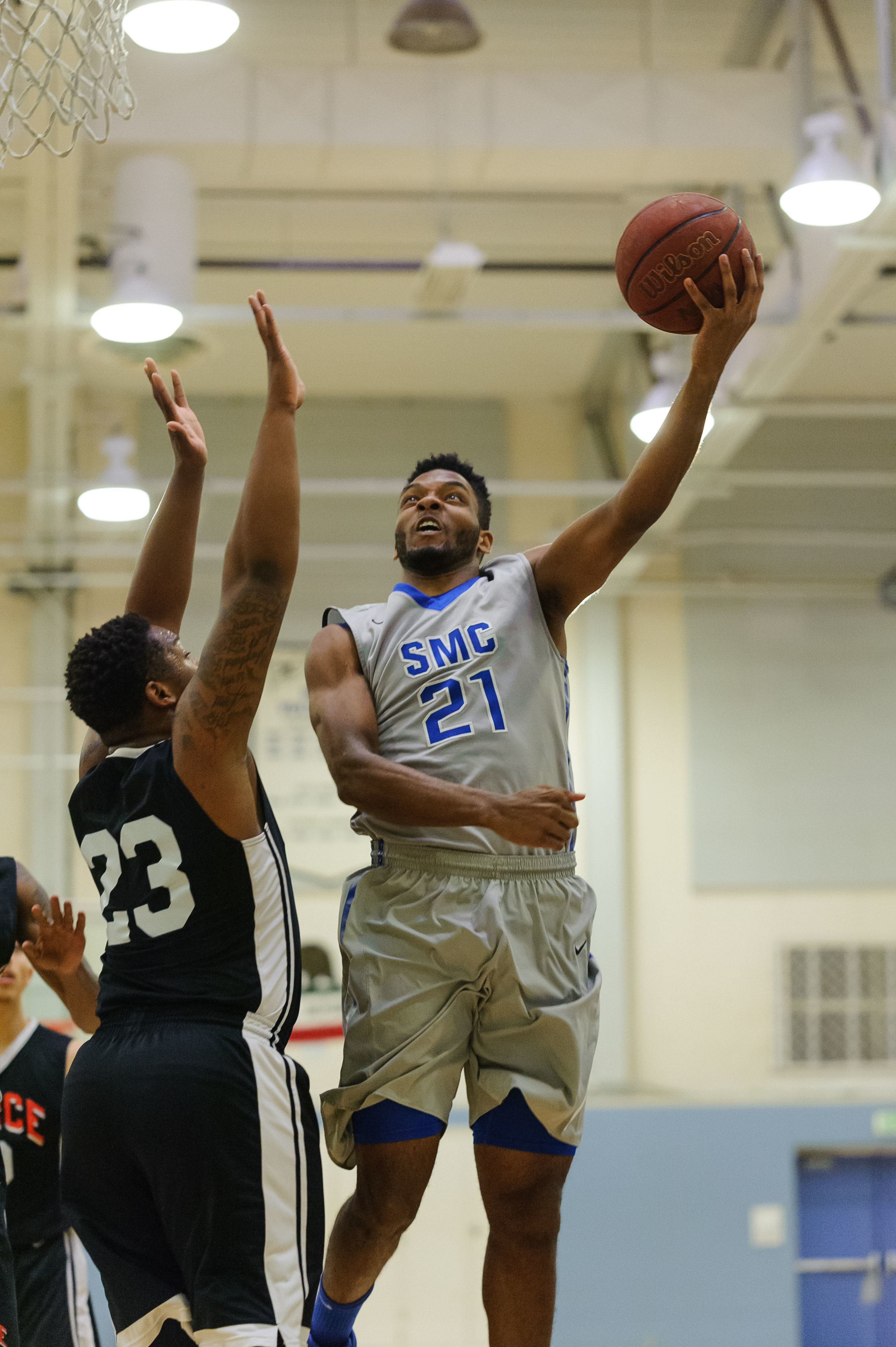  Forward Khalil Taylor (21,Right) of Santa Monica College goes up for a left-handed layup on a contest by Rashaad Johnson (23,Left) of Pierce College. The Santa Monica Corsairs lose their final game of the season 103-91 to the Pierce College Brahmas.