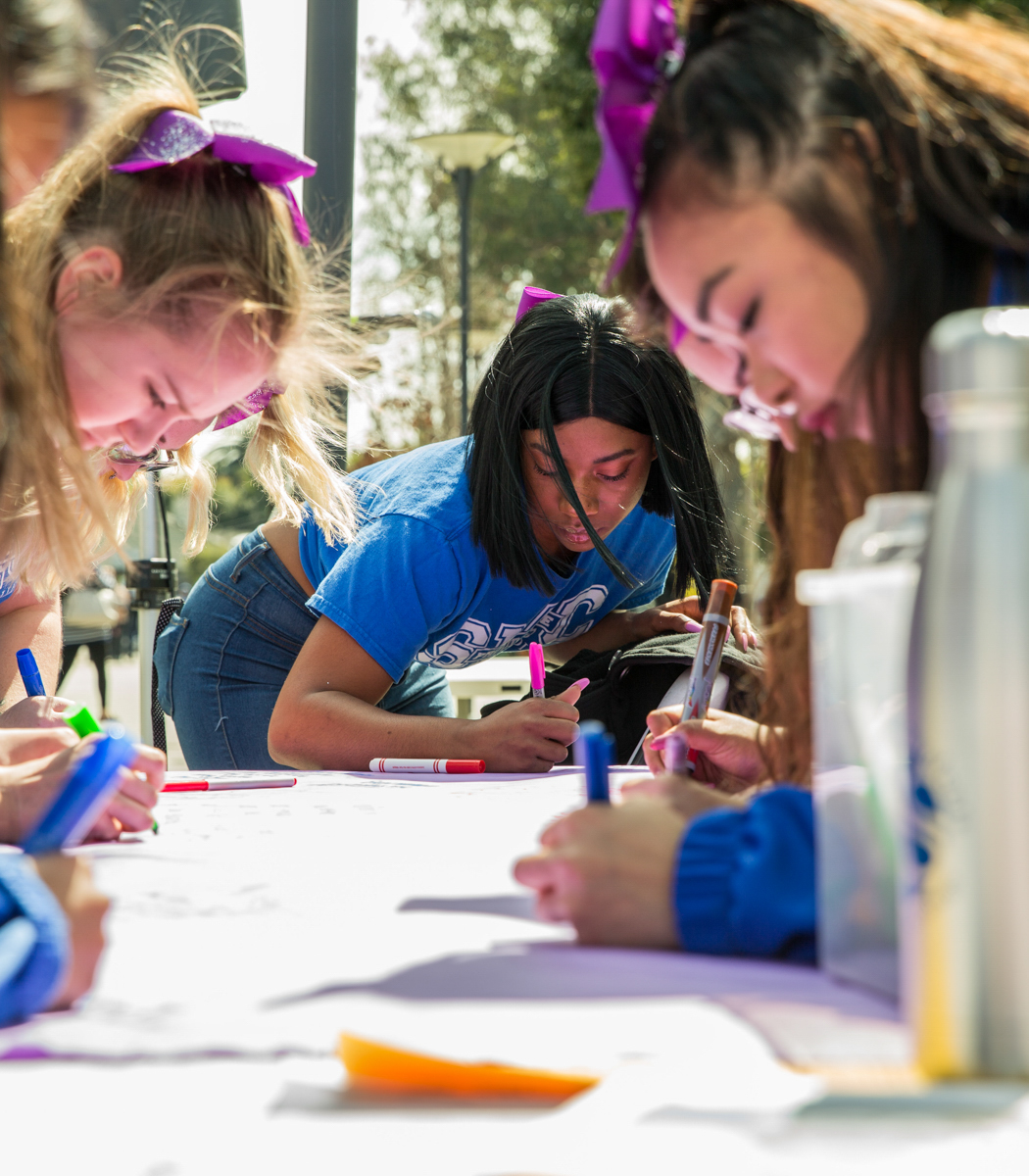  Santa Monica College (SMC) student Winnie Marcelin (center), a freshman communication studies major and a member of the SMC cheer squad, takes part in the SMC Women’s Day event by being focused while writing about the women in her life that inspire 