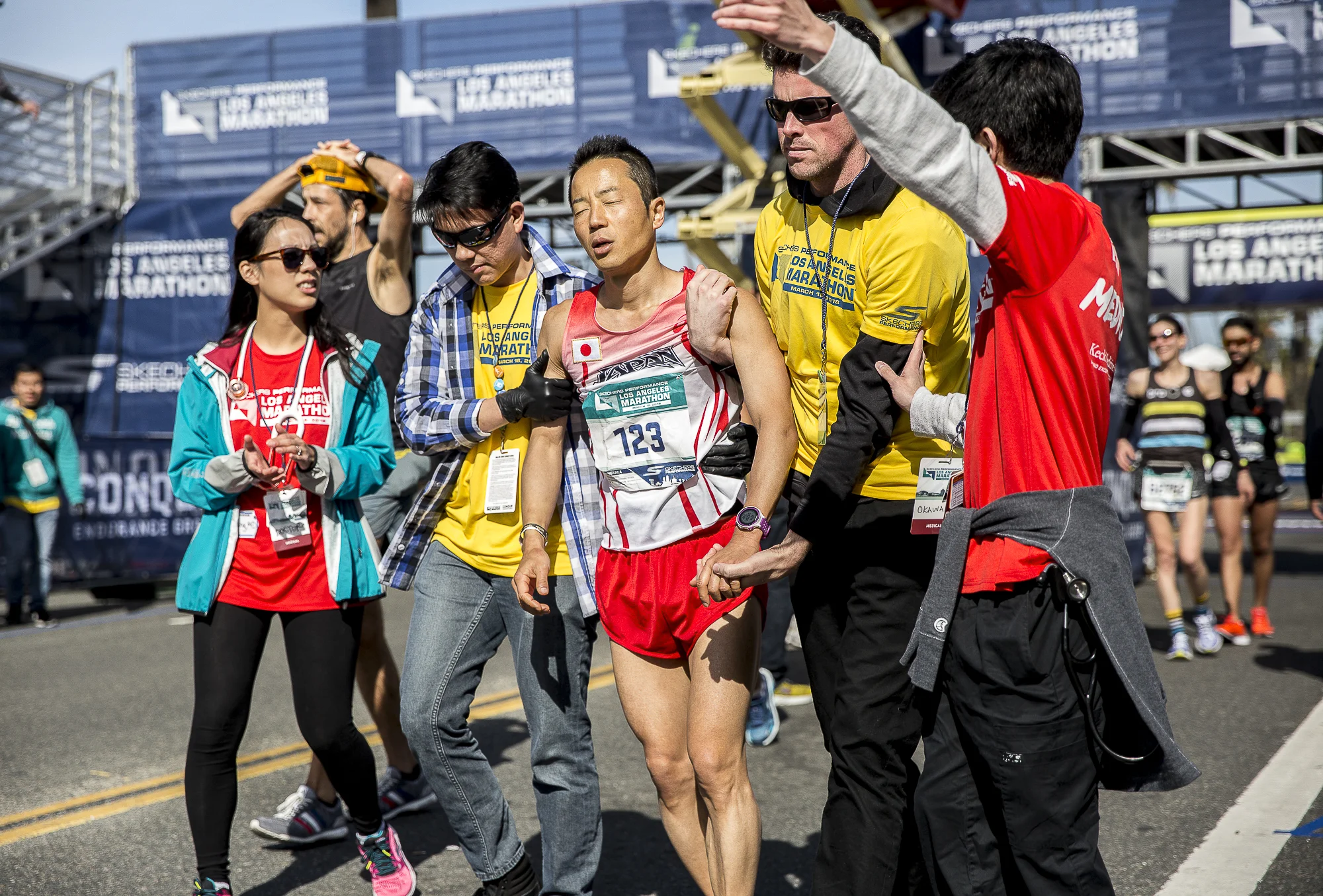 Koji Kawamoto (bib #123) receives help from “Hotwalkers” after finishing the 2018 Los Angeles Marathon with a total race time of 3:11:40 on March 18, 2018 in Santa Monica, California. “Hotwalkers” are Los Angeles Marathon volunteers who escort runners to the medical tent after finishing the event if they are showing signs of ill health. (Matthew Martin/Corsair Photo)