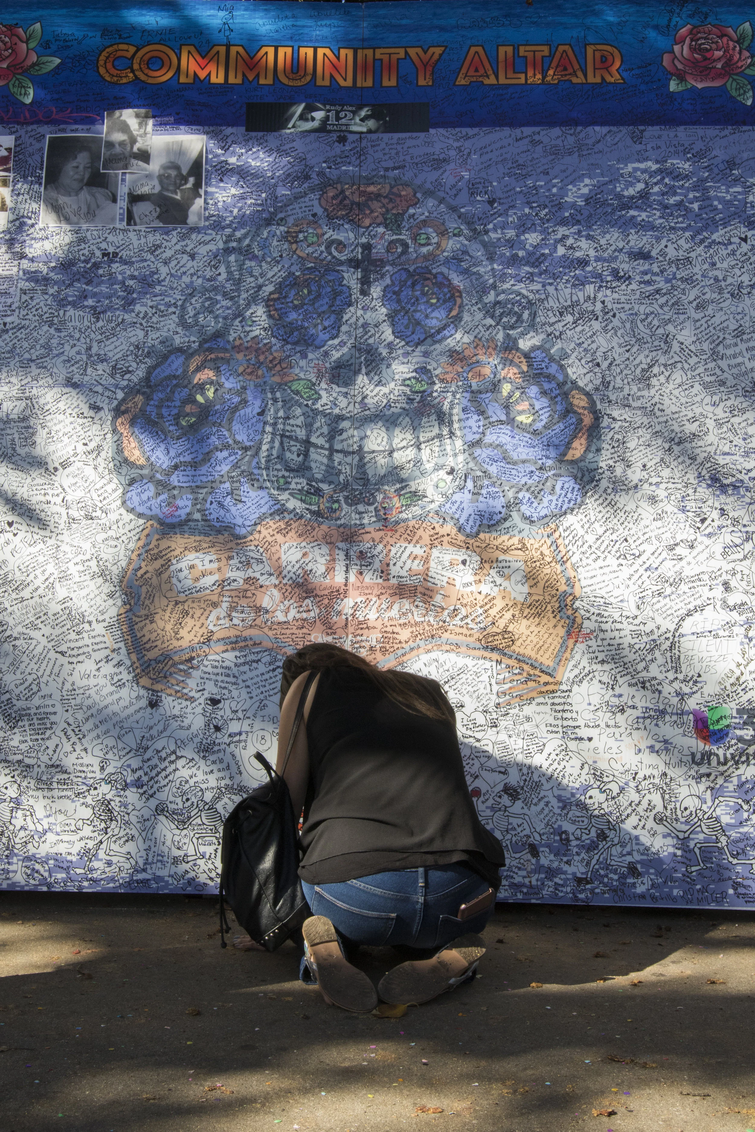A woman pays respect for her deceased loved one at the Community Altar as part of the Dia De Los Muertos festivities on Olvera Street in downtown Los Angeles, California. The community altar is a place where event attendees can write the name or leave a photo of someone close to them who has passed away. (Zane Meyer-Thornton/Corsair Photo)