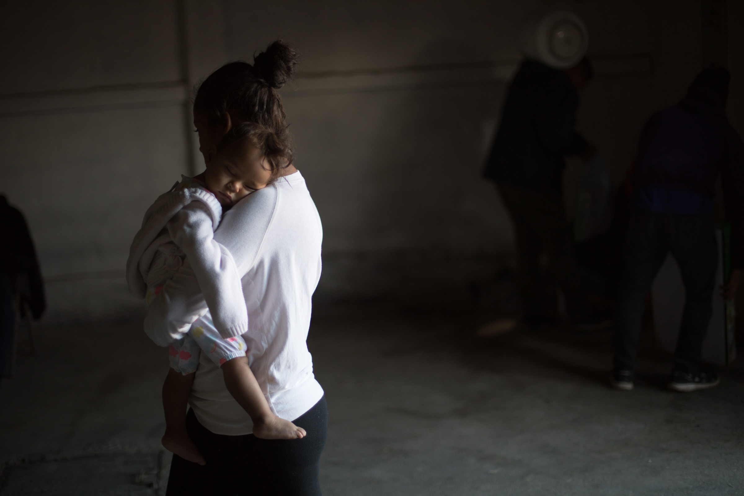   A mother carries her sleeping child into the women and children’s shelter at El Barretal in Tijuana, Mexico, Sunday, Dec. 2, 2018. The specially designated structure for women and children contains a former bar that is now a temporary dispensary of