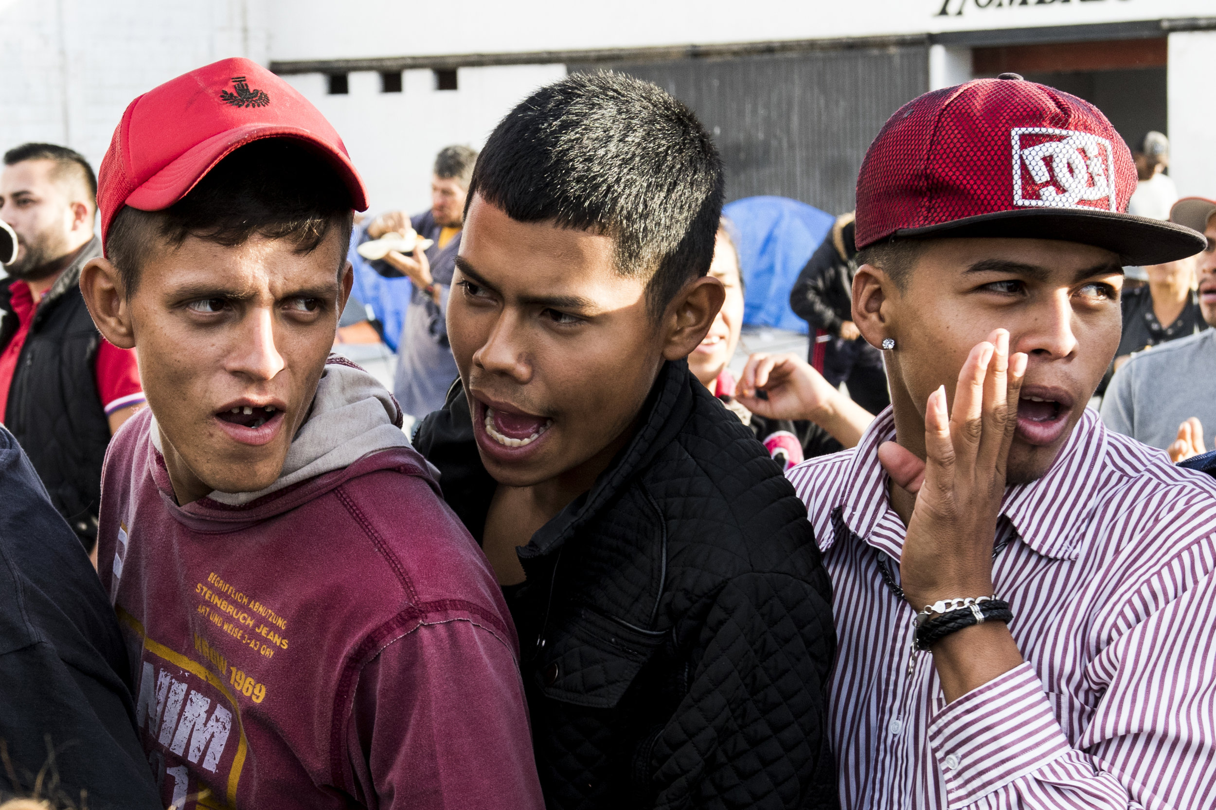   Three migrant teenage males shout to draw attention to people cutting a line for supplies at the El Barretal shelter, a former concert venue turned migrant shelter in Tijuana, Mexico, Saturday, Dec. 1, 2018. Photo By: Zane Meyer-Thornton/ Corsair C