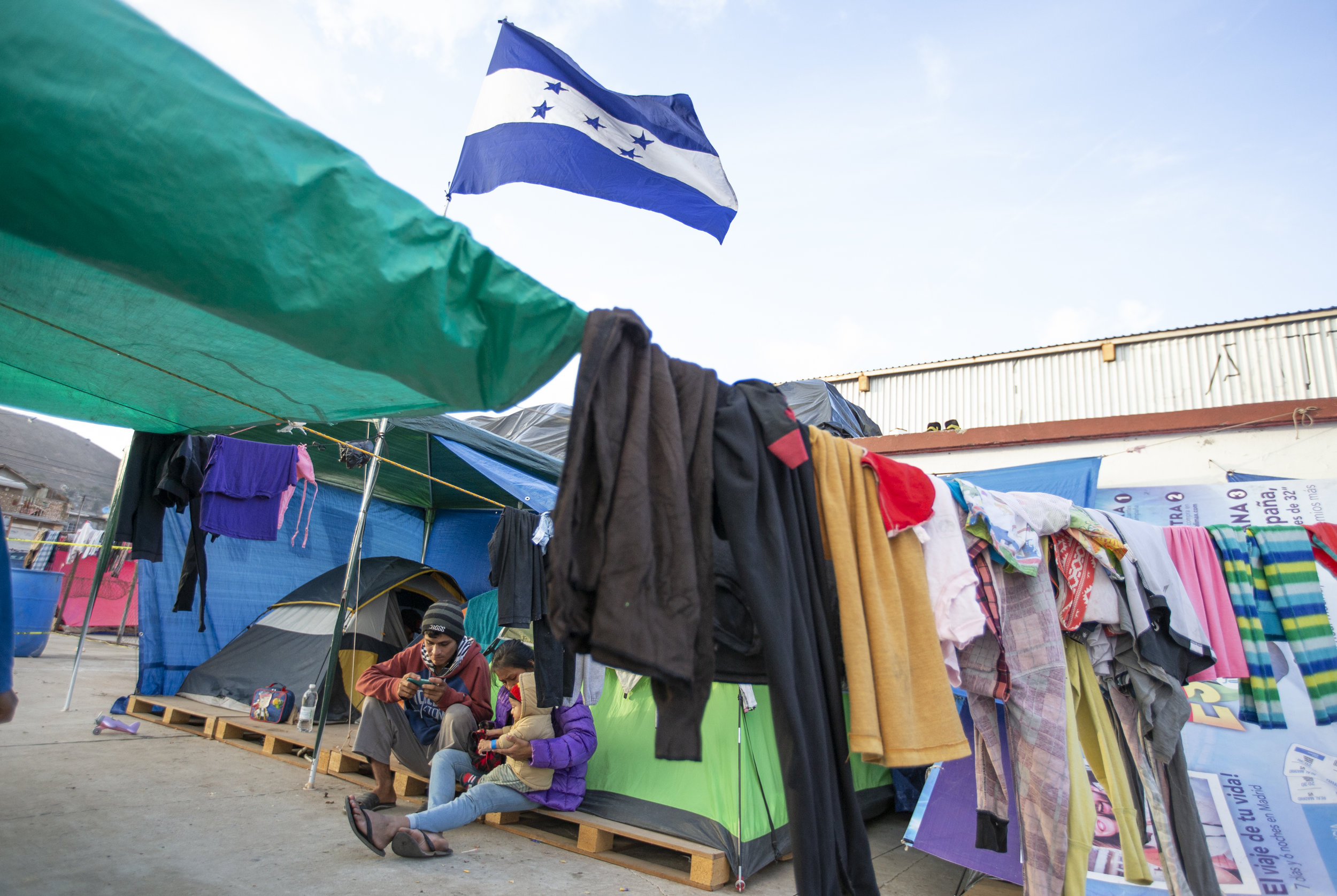   A family part of the Central American migrant caravan take shelter in tents under the National flag of Honduras at the El Barretal nightclub, turned into a temporary shelter  in Tijuana, Mexico, Saturday, Dec. 1, 2018. Photo By: Daniel Bowyer / Cor