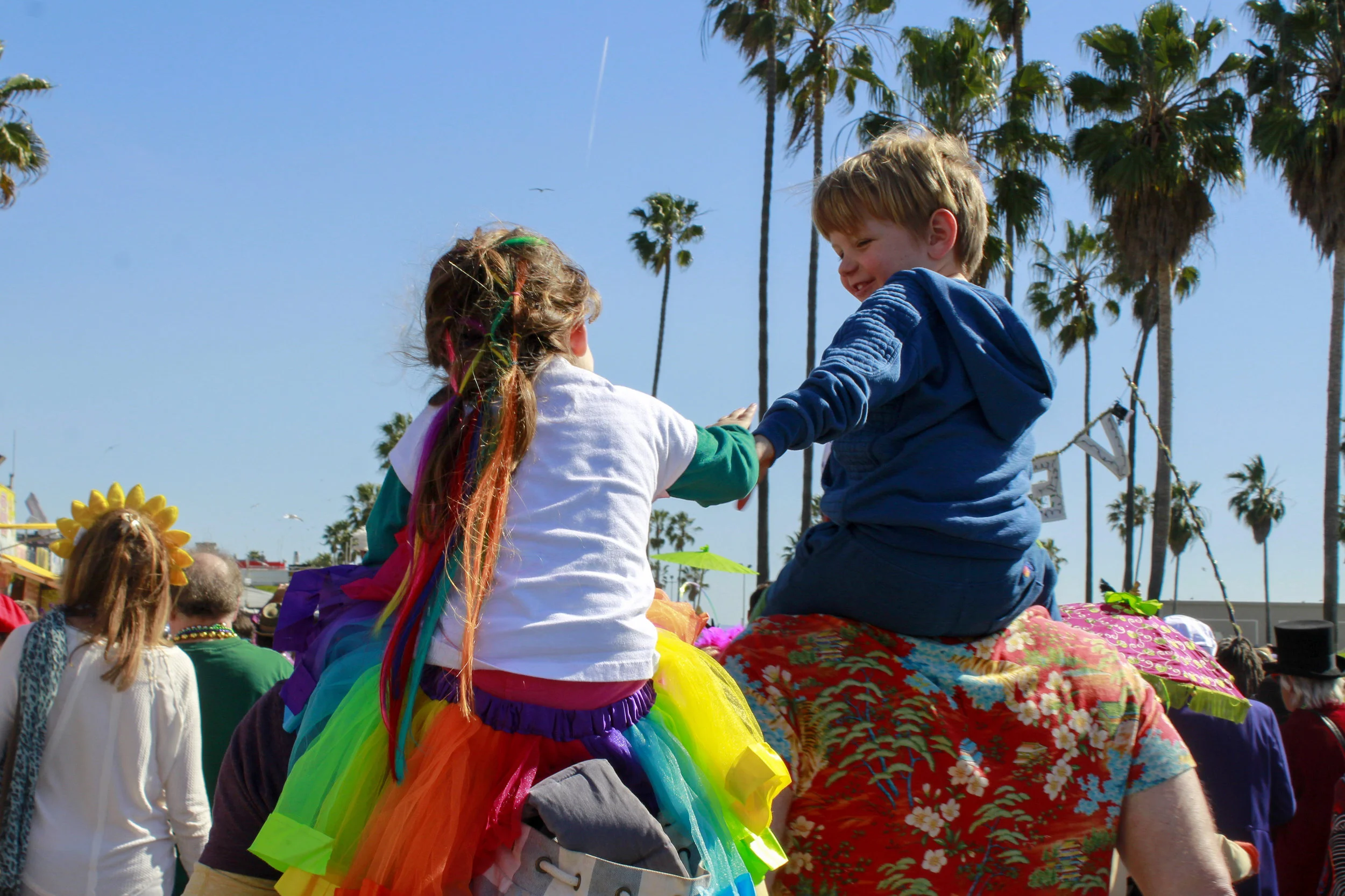 Children reach for one another as they rest on shoulders amongst the chaos of the 17th annual Venice Beach Mardi Gras parade on Feb 23, 2019 in Los Angeles, California. Photo by Danica Creahan.