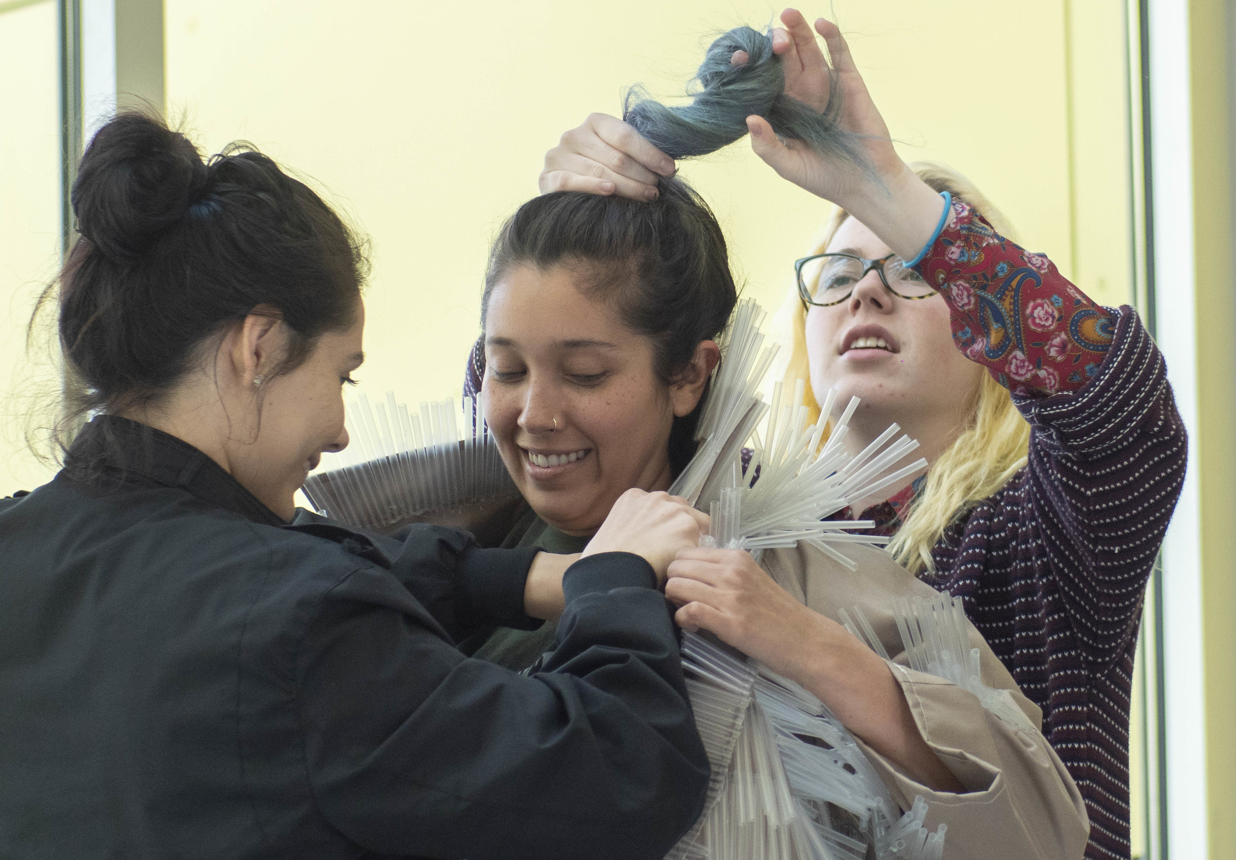 Getting by with a little help from her friends, Carla Claure (center), gets poking straws adjusted away from her cheeks by Lucia Aguilar Cole. Brooke Harrington (right), ties Claure’s hair high and safe from the prickly plastic. She wears the straw infused jacket before the short, “Straws,” screens on Thursday April 4, which is the second in the Green Screen Series, playing two more films this spring semester all of which are open to the public and free of admission. The Center for Media Design, at Santa Monica College. Santa Monica, California, 2019. (Victor Noerdlinger/Corsair)
