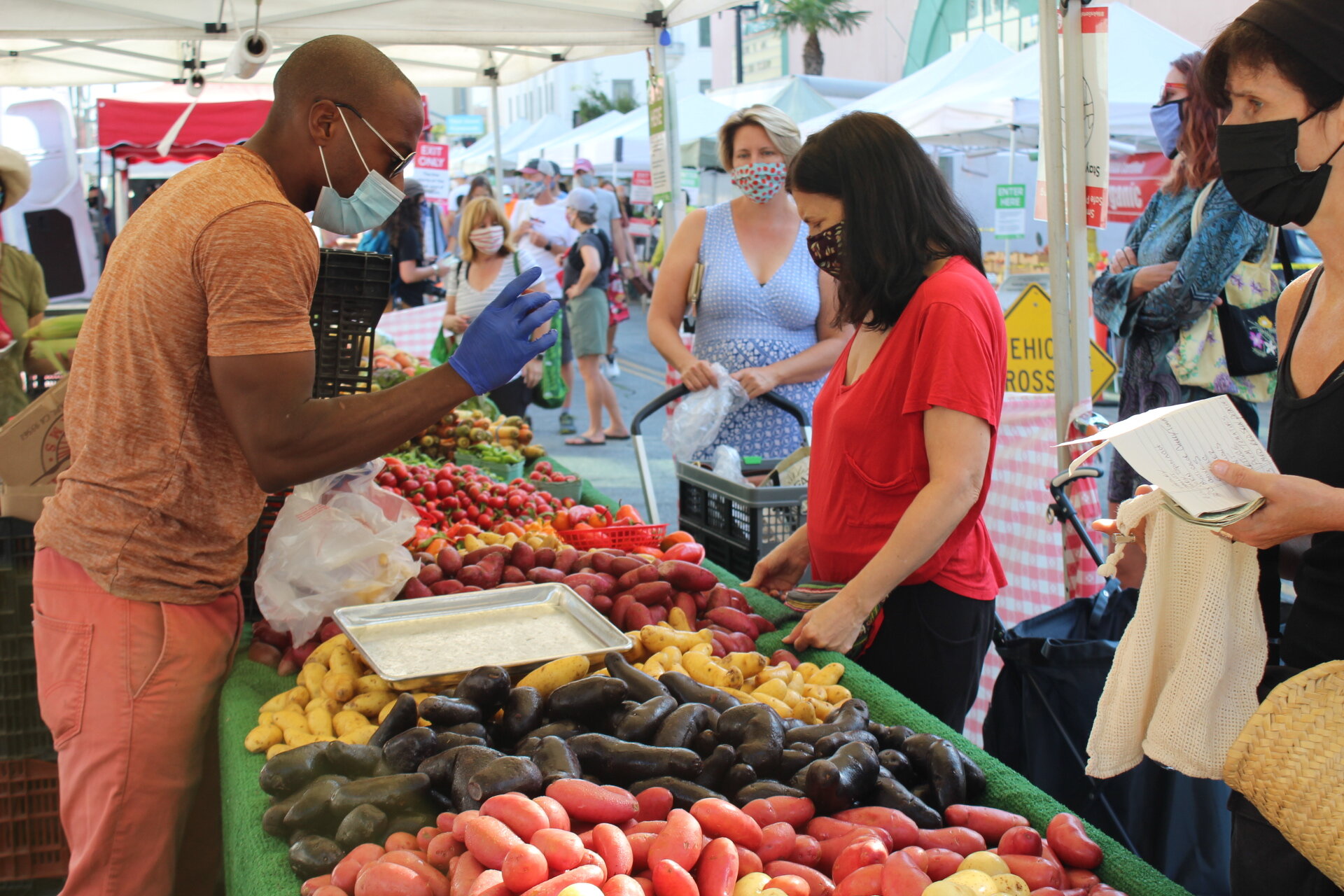   Eric Hester of Weiser Farms at the Santa Monica Farmers Market on Saturday, September 5,2020. Hester helps a customer pick out their famous magic potatoes, while wearing latex gloves and a mask. (Johaira Dilauro / The Corsair)  