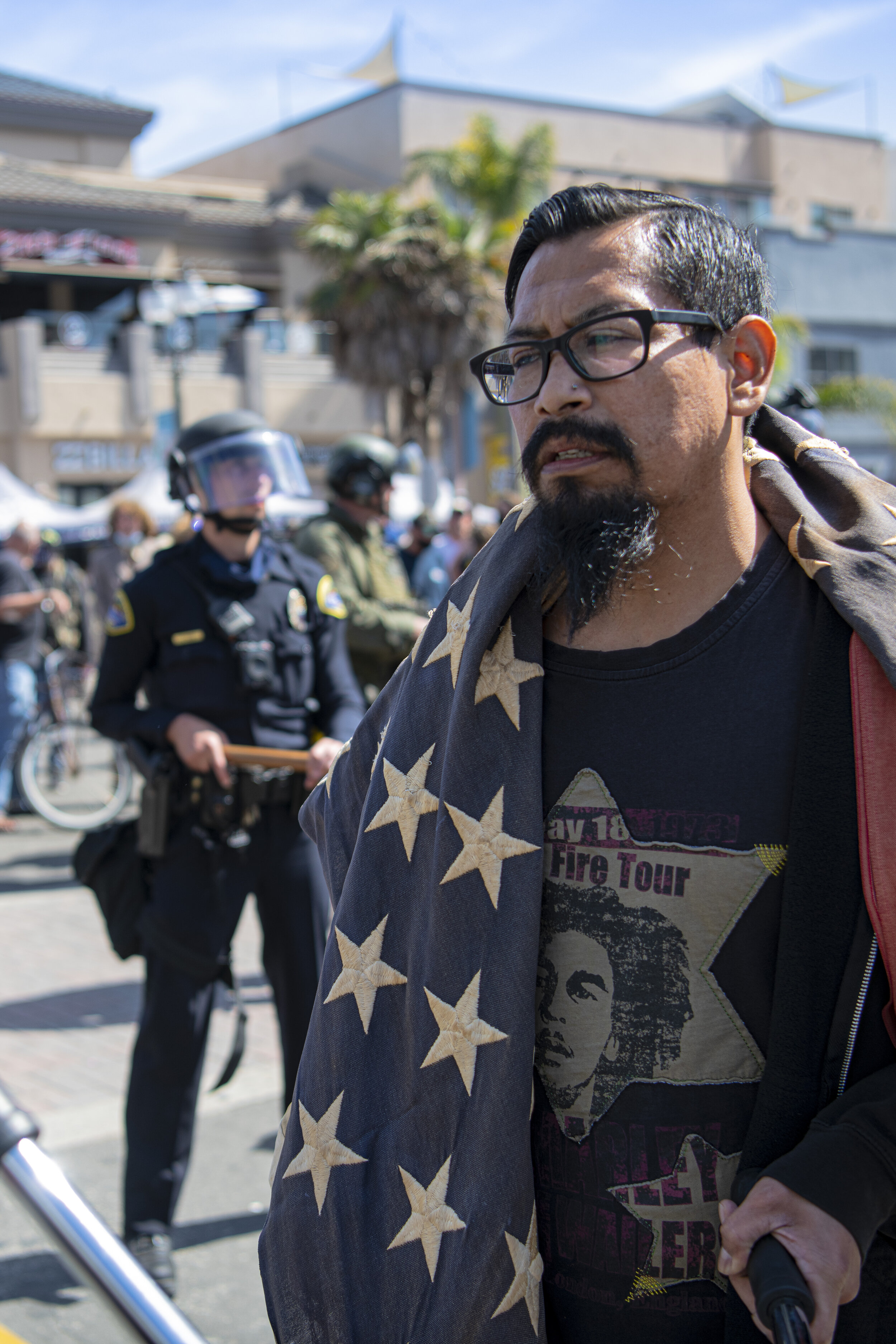  A protester walks among the swat officers with a distressed American flag at the Black Lives Matter/ White Lives Matter protest held in Huntington Beach, Calif. on March 11, 2021. (Jon Putman / The Corsair) 