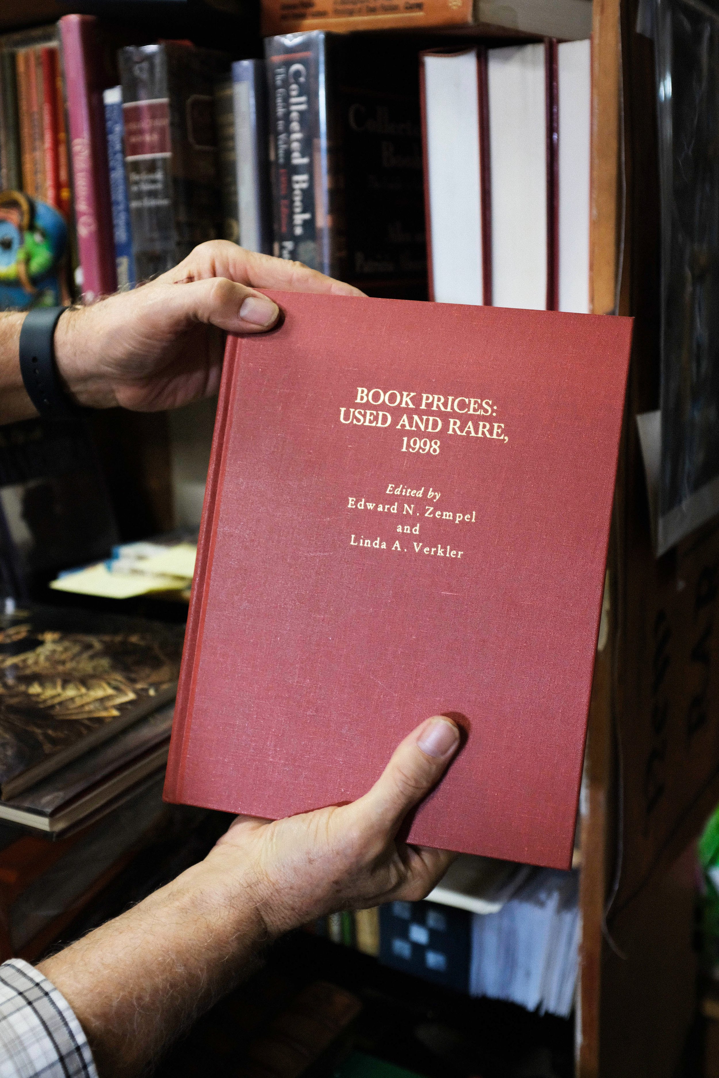  Bill Wirt holds up a reference book from 1998, of the prices of used and rare books. This is a method not used to this day, as the last copy he bought is from 1999. Bargain Books in Van Nuys, Los Angeles, California. November 19, 2021  (Anna Sophia 