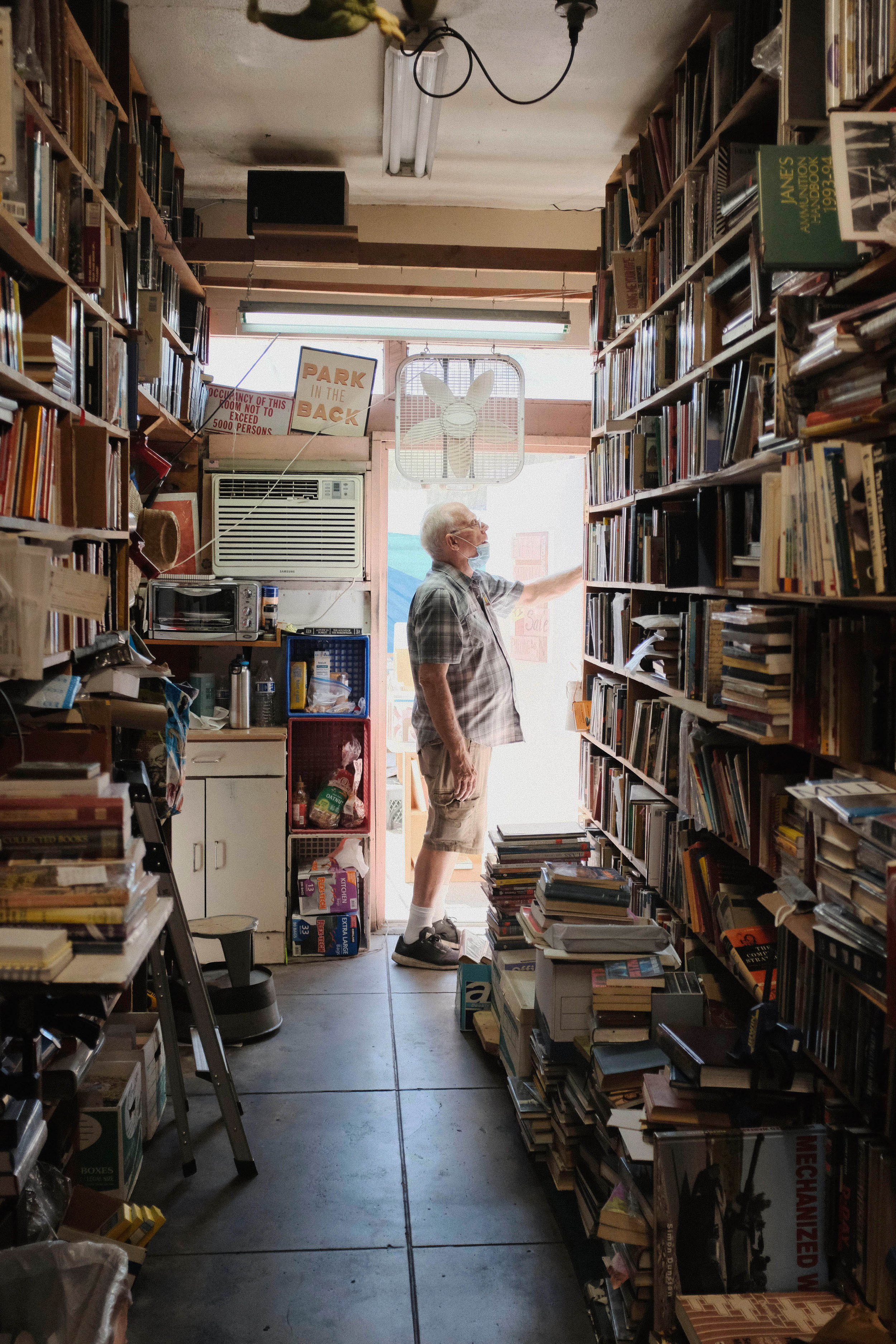  Bill Wirt walks to the back of the store, in search of a book that a customer has inquired about. Wurt first searches for a book, before asking his neice to check the stockroom. Bargain Books in Van Nuys, California. September 3, 2021 (Anna Sophia M