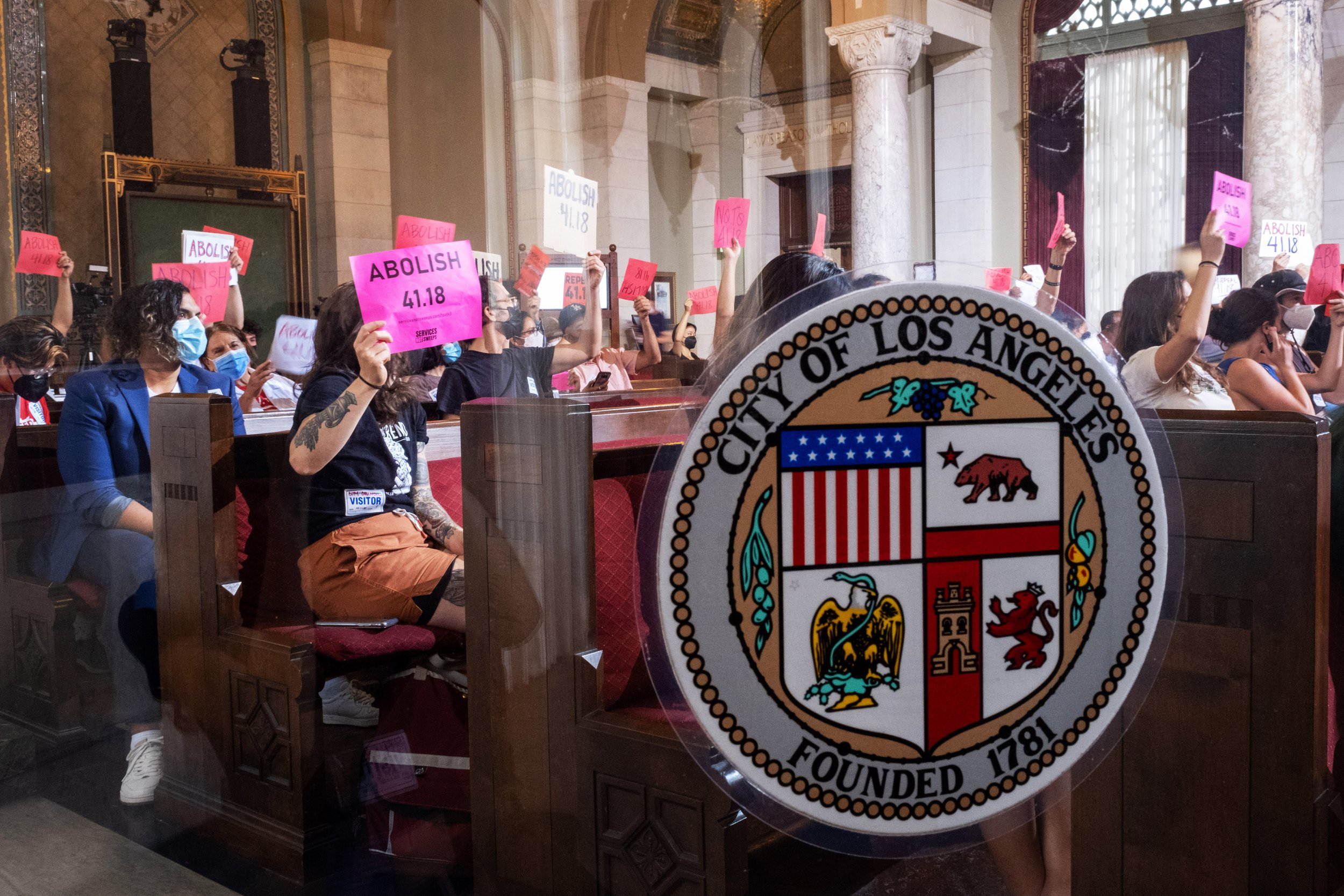  Los Angeles community members and activists gather inside of City Hall for a public hearing. The room is filled with signs and loud tones of dissent towards the new amendment to article 41.18, which would later be passed in an 11-3 vote by the Los A