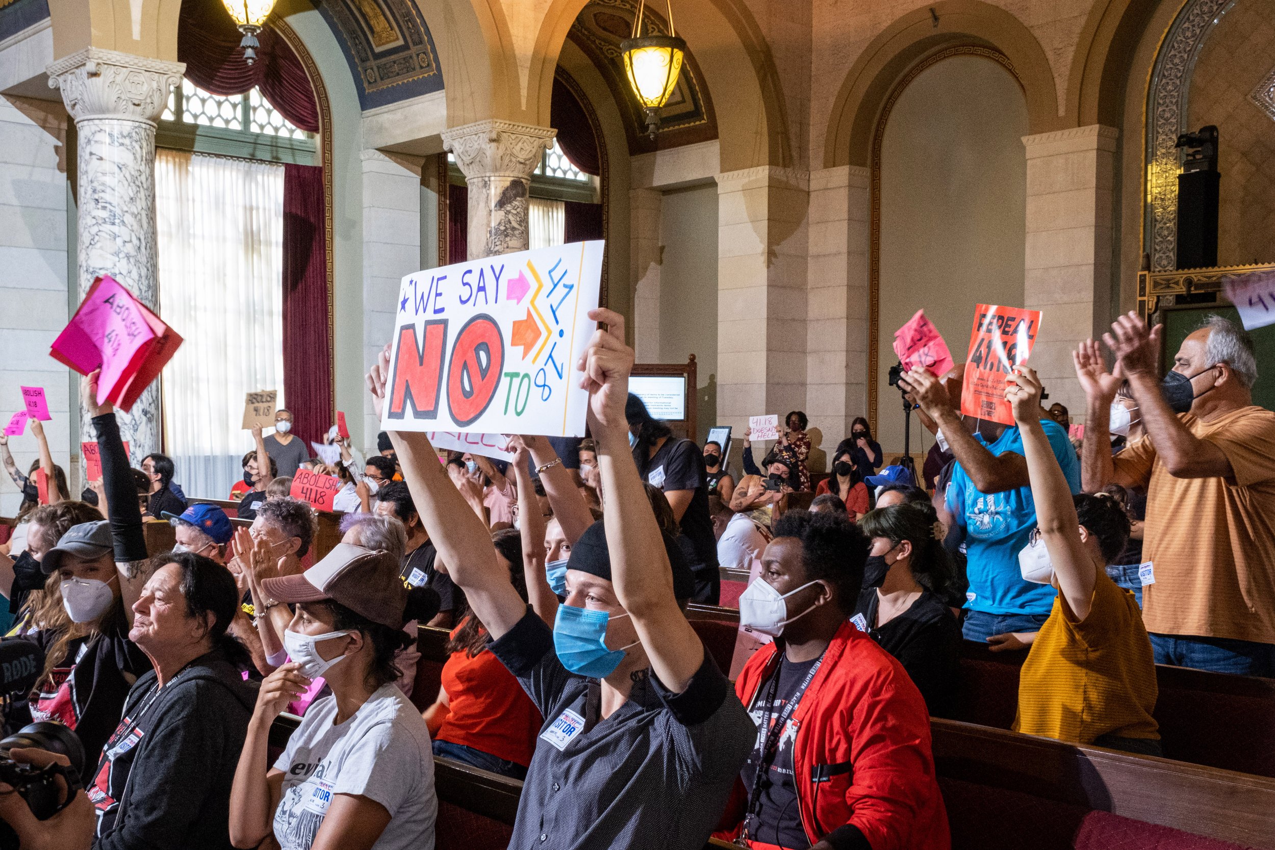  Los Angeles community members and activists gather inside of City Hall for a public hearing. The room is filled with signs and shouts in dissent of the new amendment that would later be passed in an 11-3 vote by the Los Angeles City Council members.
