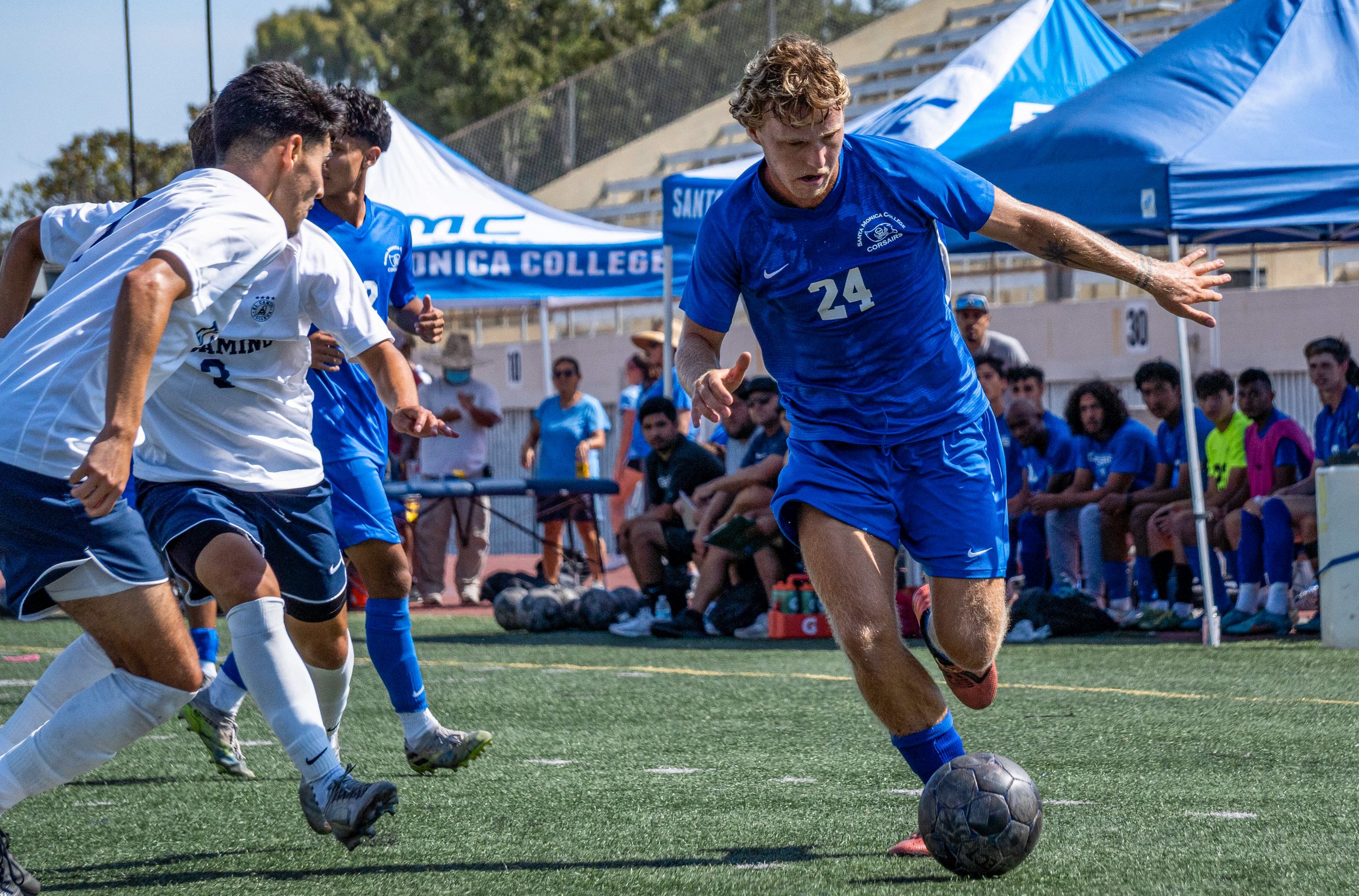  El Camino Warriors storm in from the side as Alexander Lalor (24) rushes in for a kick while his coach and the teammates watch anticipatedly from the sidelines. Lalor later scored SMC’s first goal during the matche’s first half. The Corsair Field in