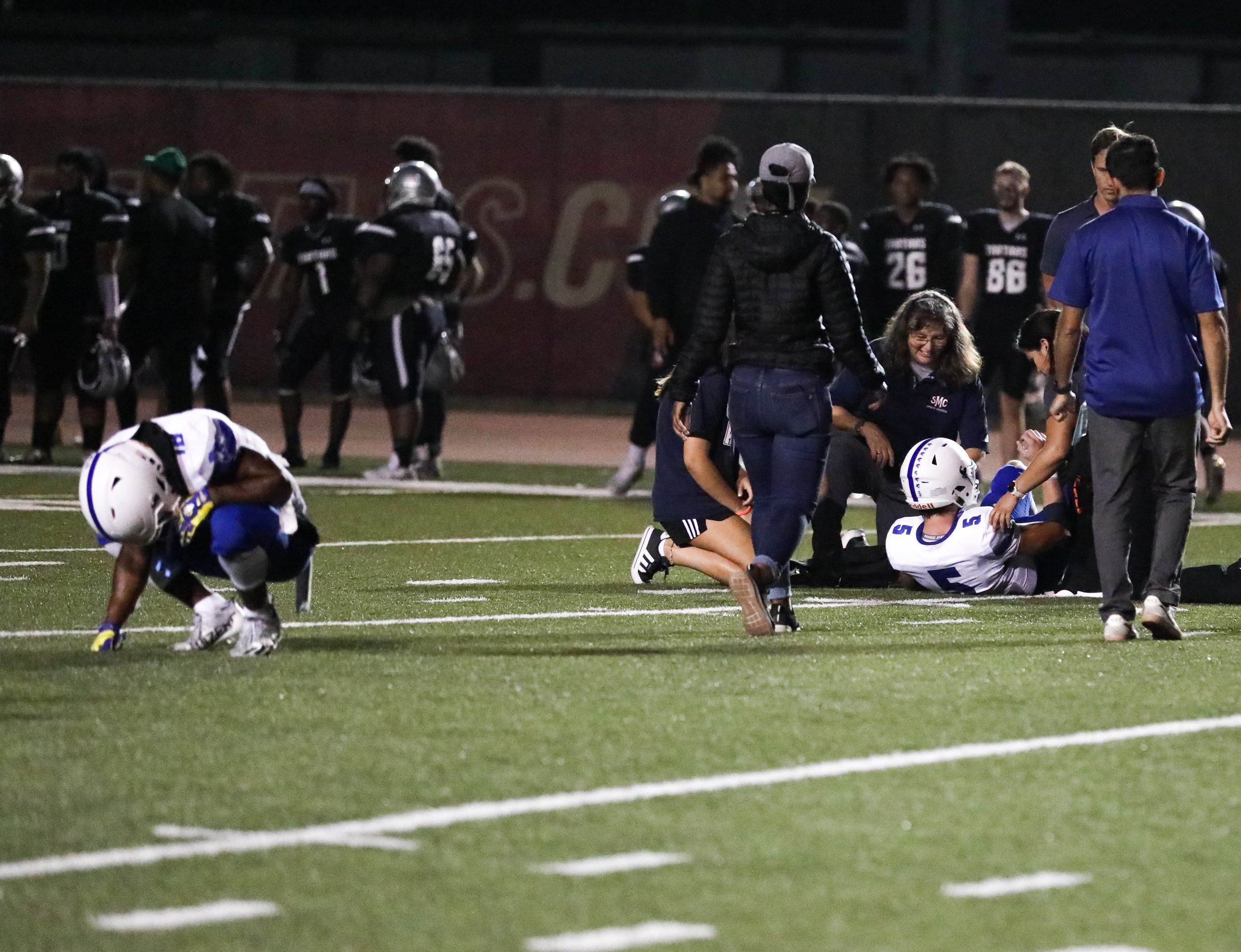  Santa Monic College Wide Receiver Everson Bozeman (18, L) squatting down as Quarterback Forrest Brock (5,R) being aided up from the field by the medical team after the end of a play against the Compton College Tartars on Saturday, Sept. 17 at Compto