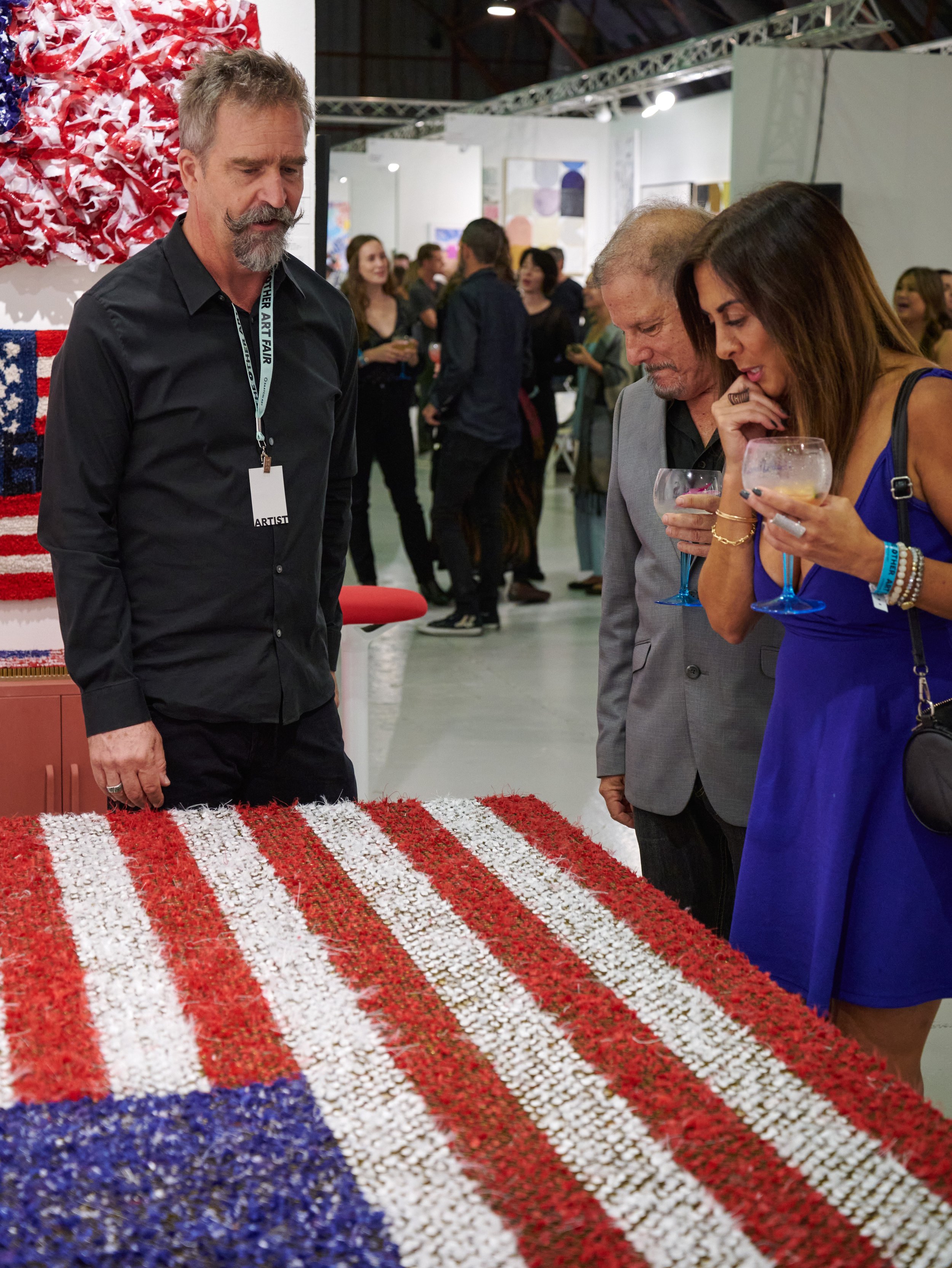  Artist Sol Hill discusses his work, "Caseload," with attendees Chris Dellorco and Marjan Khonsari at The Other Art Fair on Thursday, Sept. 22, 2022, at The Barker Hangar in Santa Monica, Calif. (Nicholas McCall | The Corsair) 