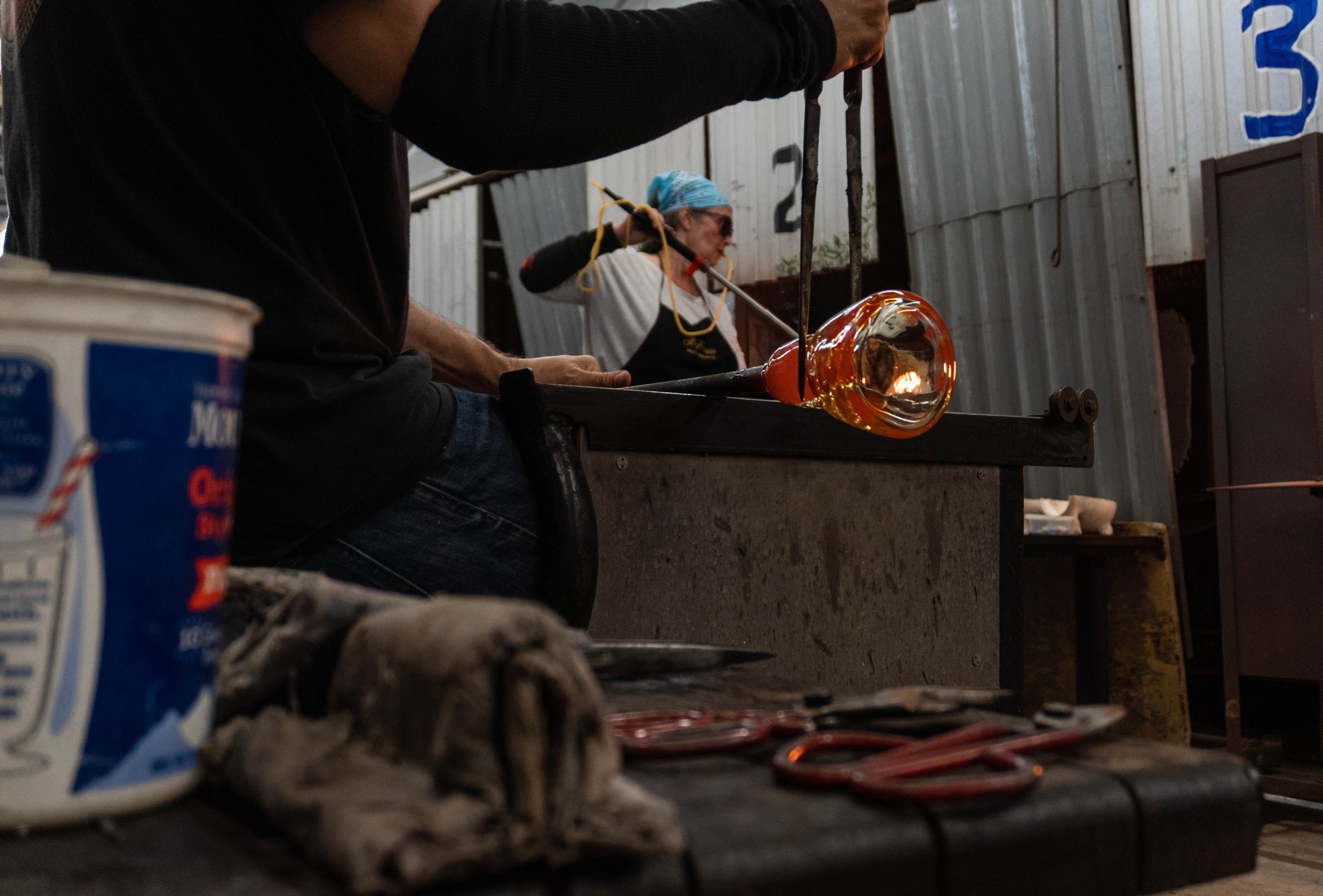  Dave Gaeta joined the Glass Sculpting class 6 weeks ago and is currently working on his in-class assignment to create a bowl. In the background, student Alexis Daniels stands by the furnace and blows into her blowpipe. Glass Sculpturing classes can 