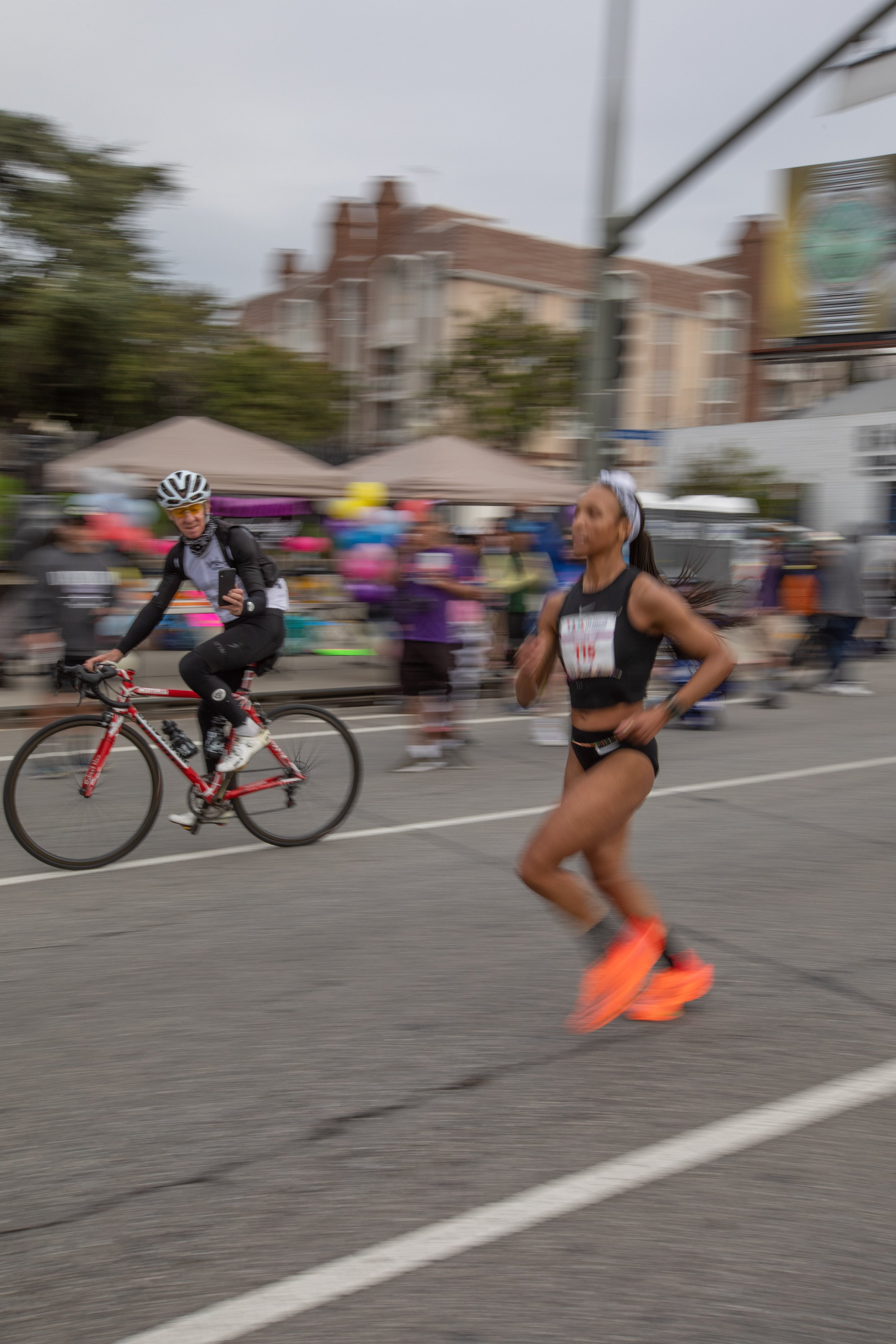  American Sharada Maddox from Los Angeles running on Santa Monica Blvd. being recorded by a cyclist admirer heading West just passing through cheers on mile 19 during the L.A. Marathon 2023. Maddox placed in seventh position on Sunday, March 19, 2023