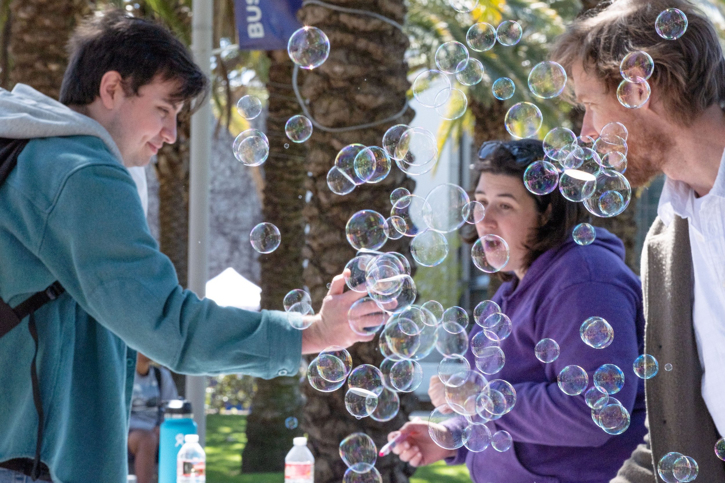  From L to R, Conor O'Sullivan, Film and Media Studies major chats with Art Department faculty Briana Simmons  and Carlson Hatton amidst a cloud of bubbles on the Quad at Motivational Madness, an event for students to relax and take a break from stud