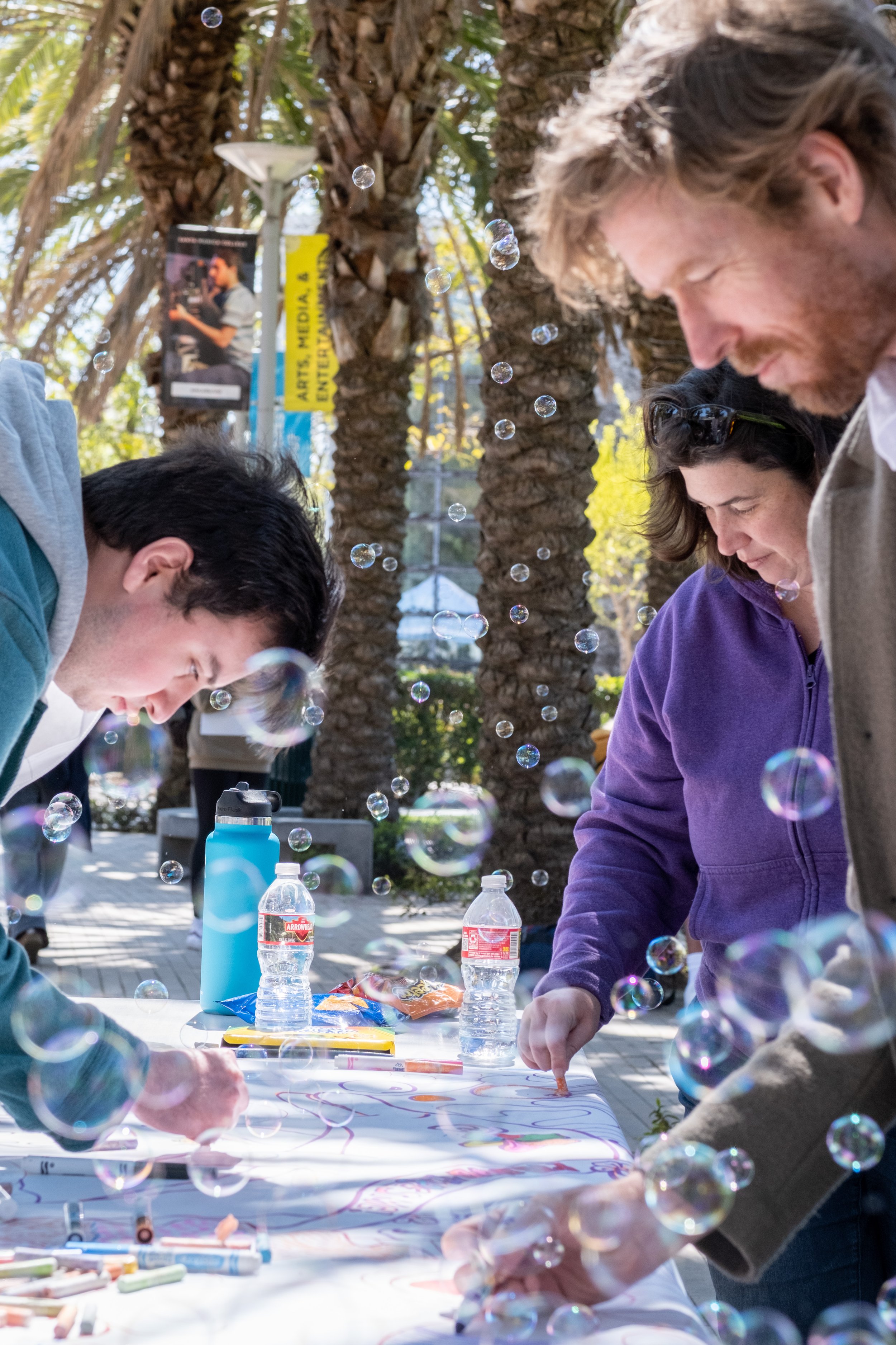  From L to R, Conor O'Sullivan, Film and Media Studies major colors on an art project with Art Department faculty Briana Simmons  and Carlson Hatton amidst a cloud of bubbles on the Quad at Motivational Madness, an event for students to relax and tak