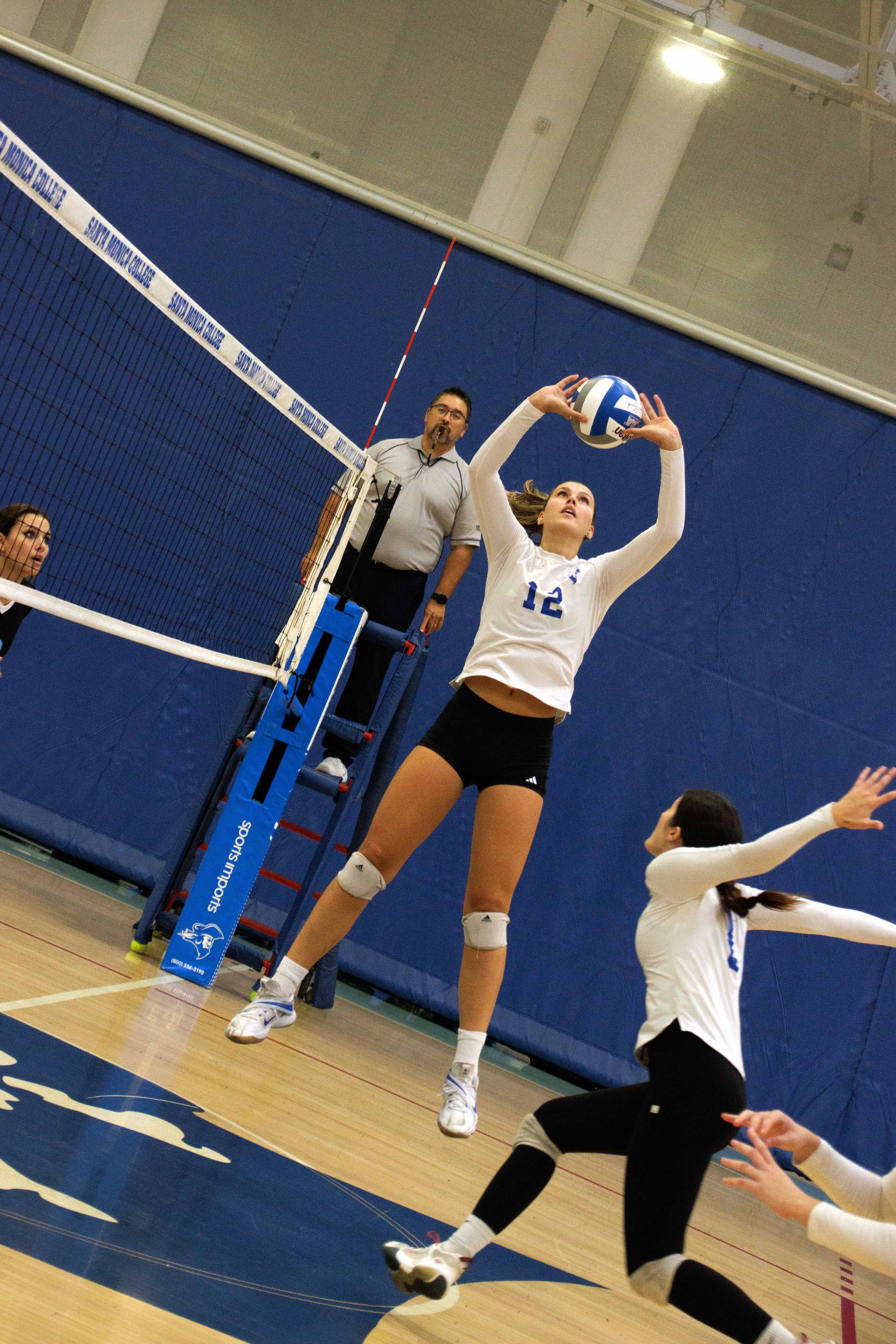  Setter Mia Paulson, number 12, performs an overhead pass to set up an attack for outside hitter Maiella Riva, number 1, during the match between Santa Monica College (SMC) and San Diego Miramar Women's Volleyball team at the SMC gymnasium, Santa Mon