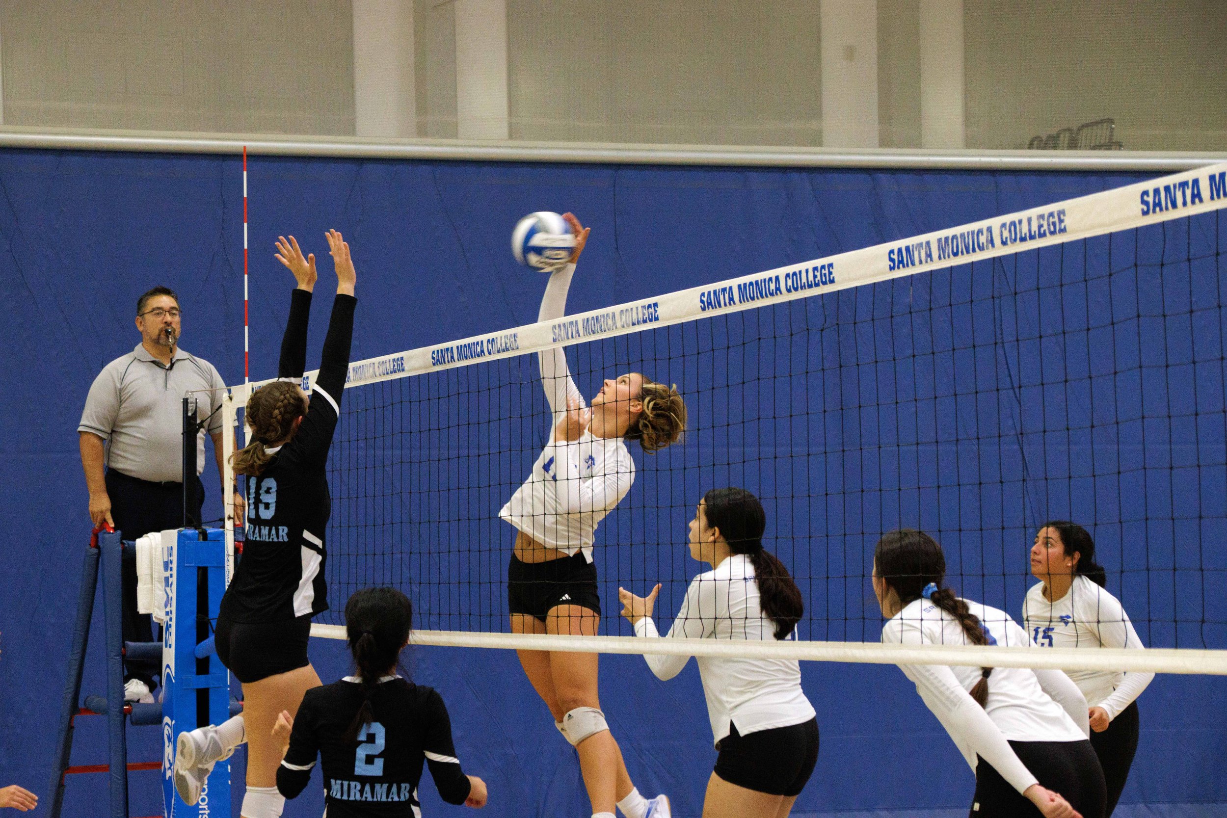  Setter Mia Paulson, number 12, center, of Santa Monica College (SMC) Women's Volleyball, hits the ball, performing an attack while number 19 of San Diego Miramar tries to block it at the SMC gymnasium, Santa Monica, Calif. on Sept. 08, 2023. (Dannie
