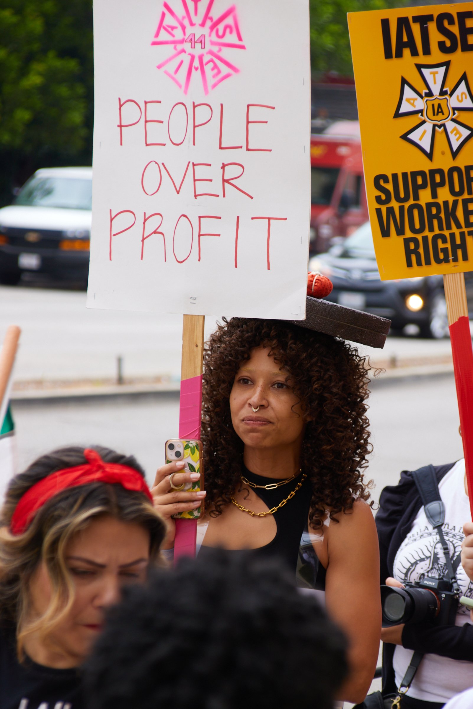  An IATSE member holding up a sign with "PEOPLE OVER PROFIT" written on and IATSE 44 logo marches in solidarity alongside SAG-AFTRA members during the SAG-AFTRA strike in front of Warner Bros. Studio Gate 3, Burbank, Calif., on Sept 29, 2023. (Dannie