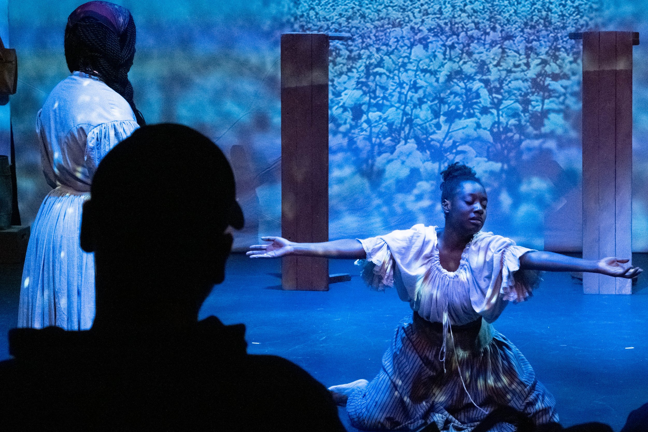  (L) Tia Jiji stands observing Raven Smith (R) perform a dance in front of a backdrop depicting cotton fields on Tuesday Oct. 17th, 2023 in Santa Monica, Calif. at the Santa Monica Colllege Studio Stage during the play "By The River Rivanna". The sil