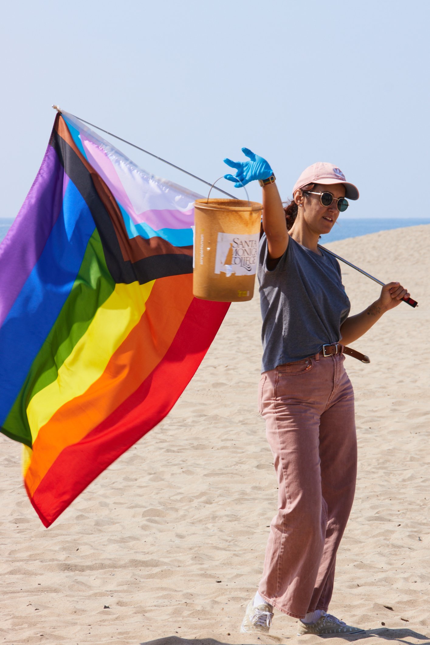  Volunteers Elif Sekman raises her bucket filled with collected trash while holding a pride flag on the other hand during a coastal beach cleanup organized by Santa Monica College Sustainability Center at The Inkwell, Santa Monica, Calif., on Sept 23