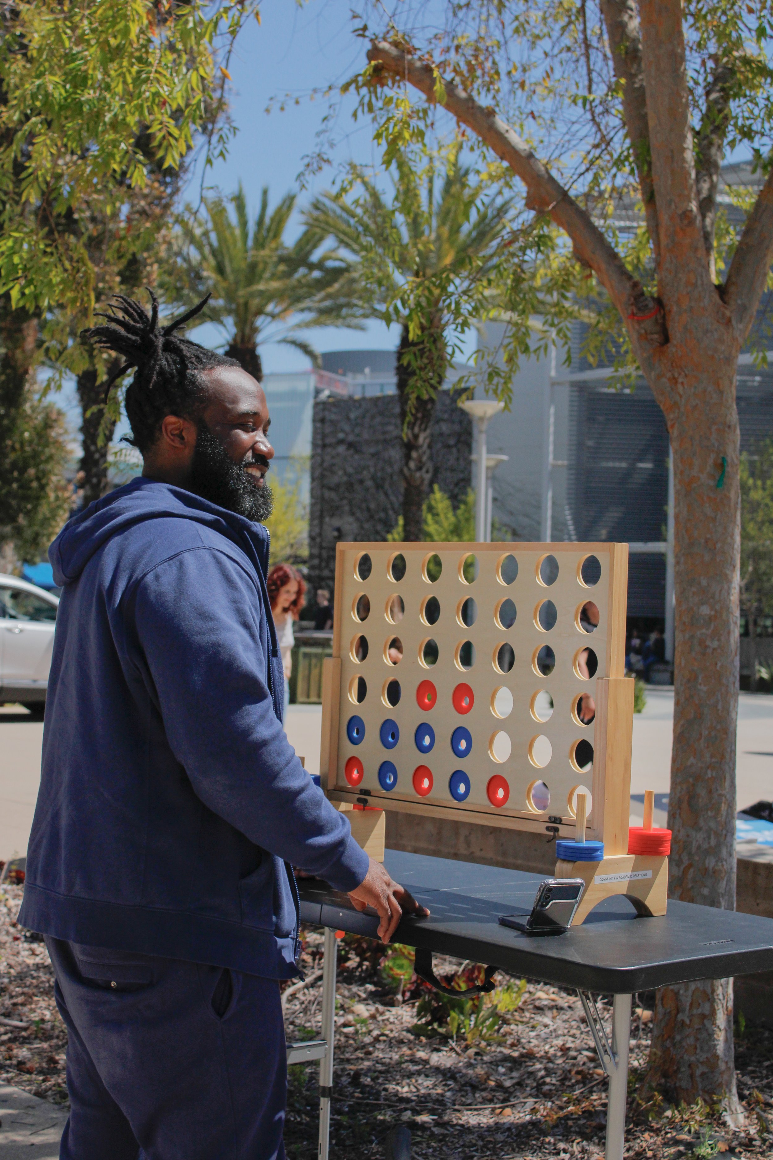  Ahmad Diakite hanging out on campus in front of a large connect four set up as a two games of corn hole unfold in front of him at Midterm Motivation day.  