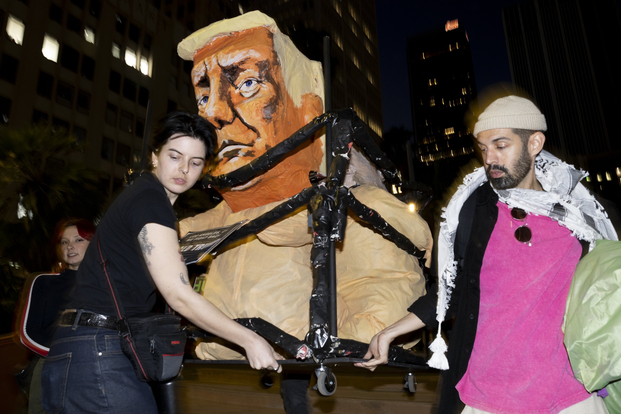 Protesters move a statute of Donald Trump, Elon Musk, and Jeff Bezos down the steps at Pershing Square in downtown Los Angeles, Calif., on Monday, January 20, 2025, during the We Fight Back protest to call for the “defeat of Trump’s Extreme-Right Bi