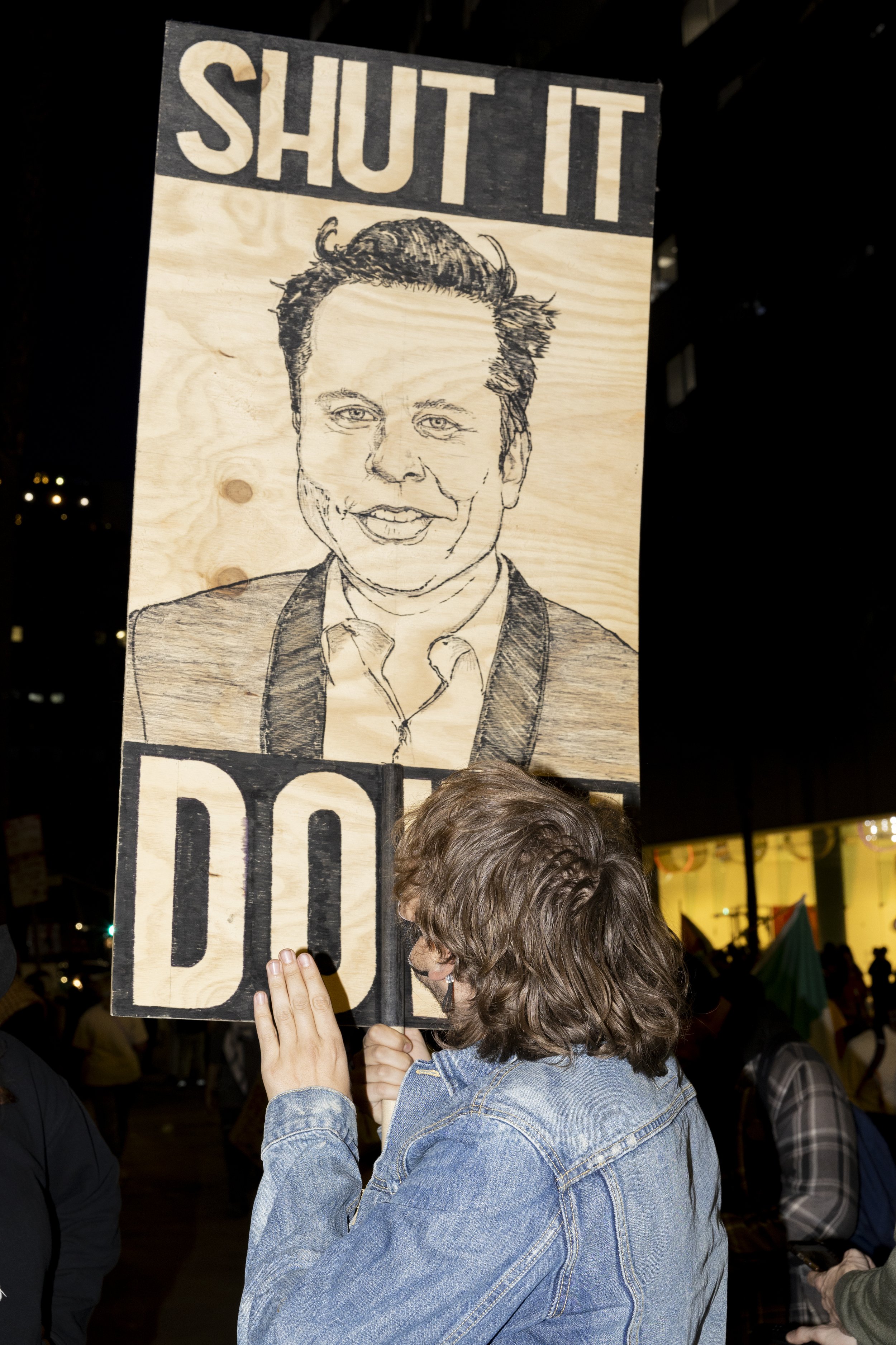 A protester holds a sign with Elon Musk on one side and Luigi Mangione on the other with the message written, “Shut it down,” on the sign, during the We Fight Back protest with the message of calling for the “defeat of Trump’s Extreme-Right Billiona