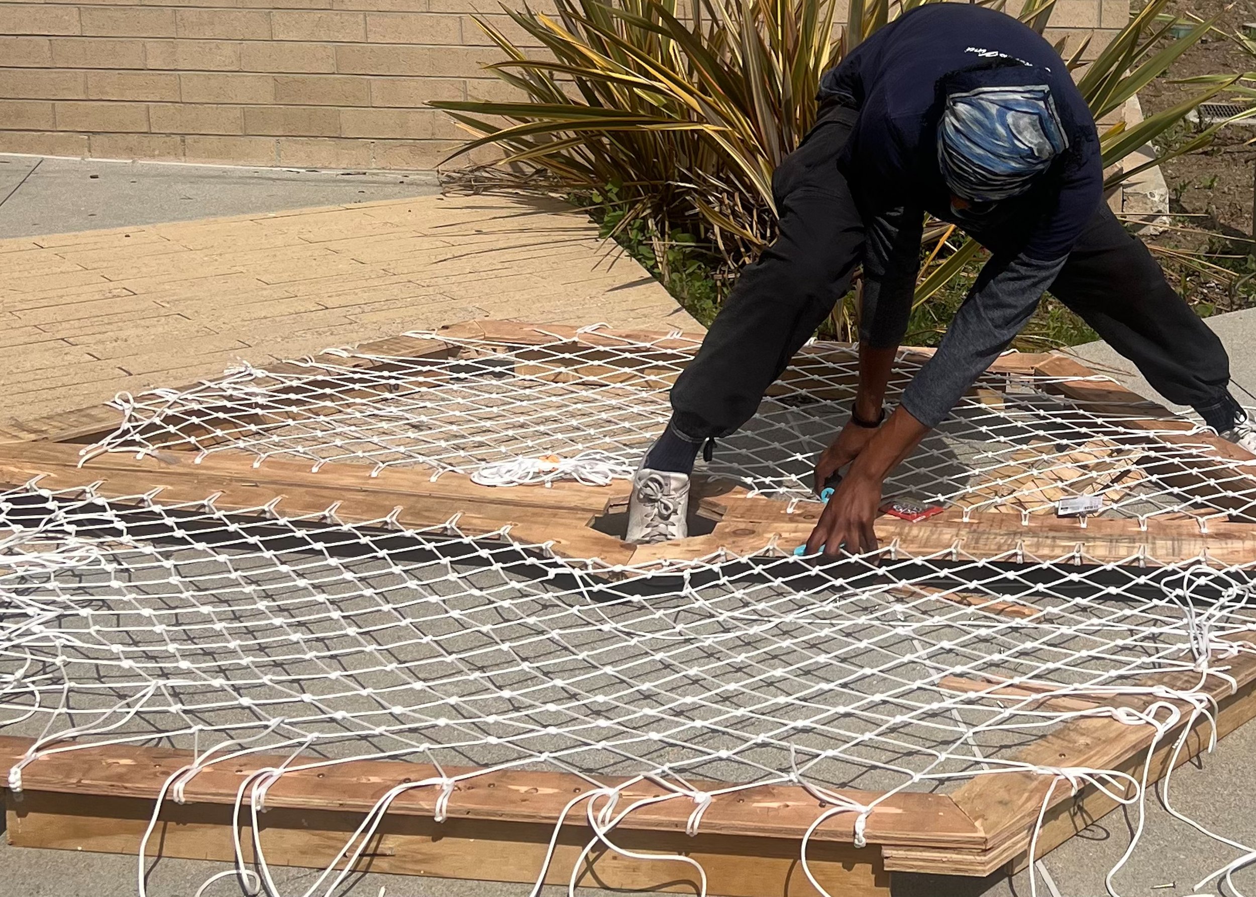River Jordan, a student from the Department of Architecture at Santa Monica College (SMC), fastens sections of a rope net onto a hexagonal wooden frame for their project for "Team Tentsion" in the Design Village Competition at the SMC Center for Med