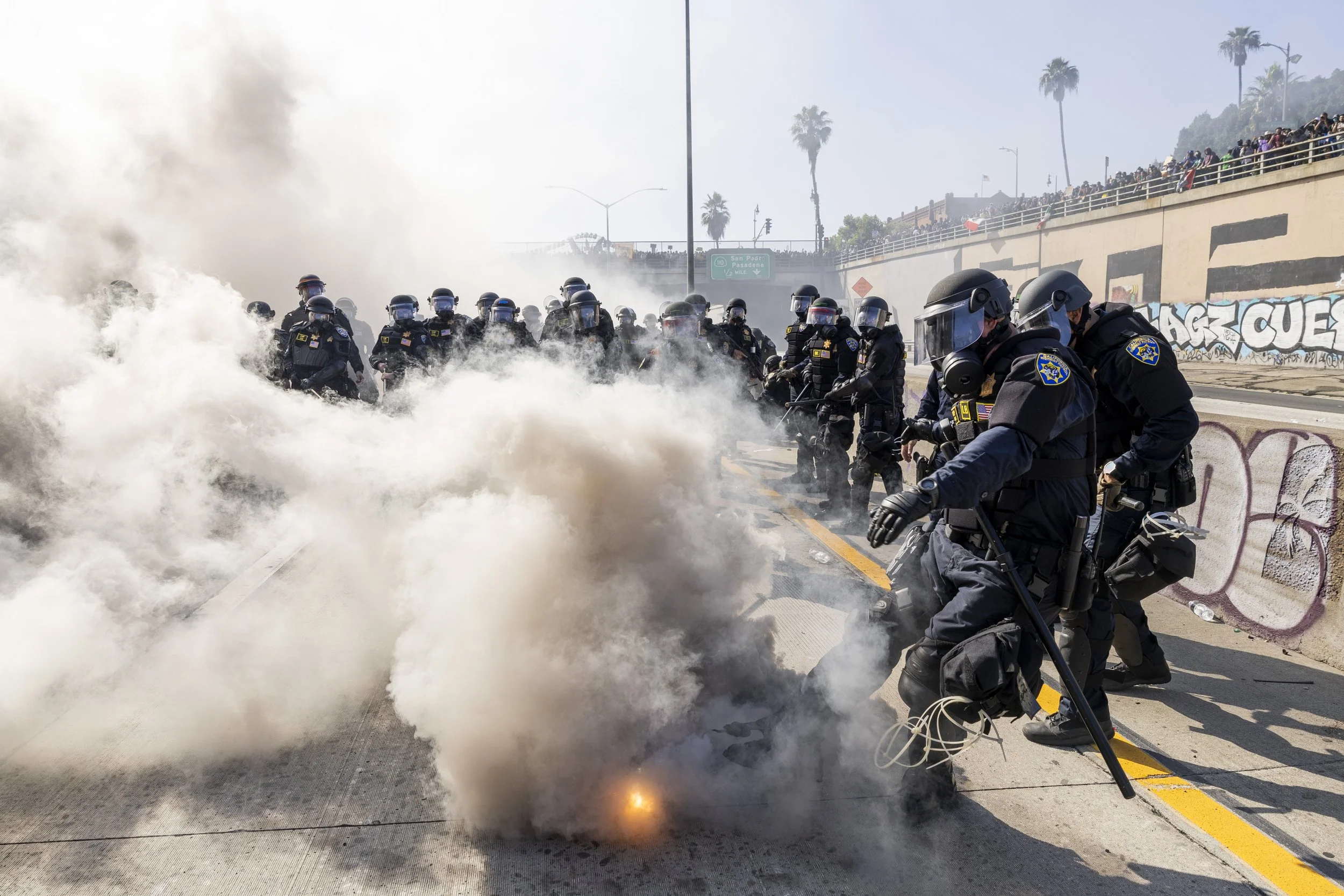 A California Highway Patrol Officer kicks back a smoke cannister after protesters kicked it back into the police line while pushing back protesters off Highway 101 in Downtown Los Angeles, Calif., deploying less than lethal ammunition and tear gas i