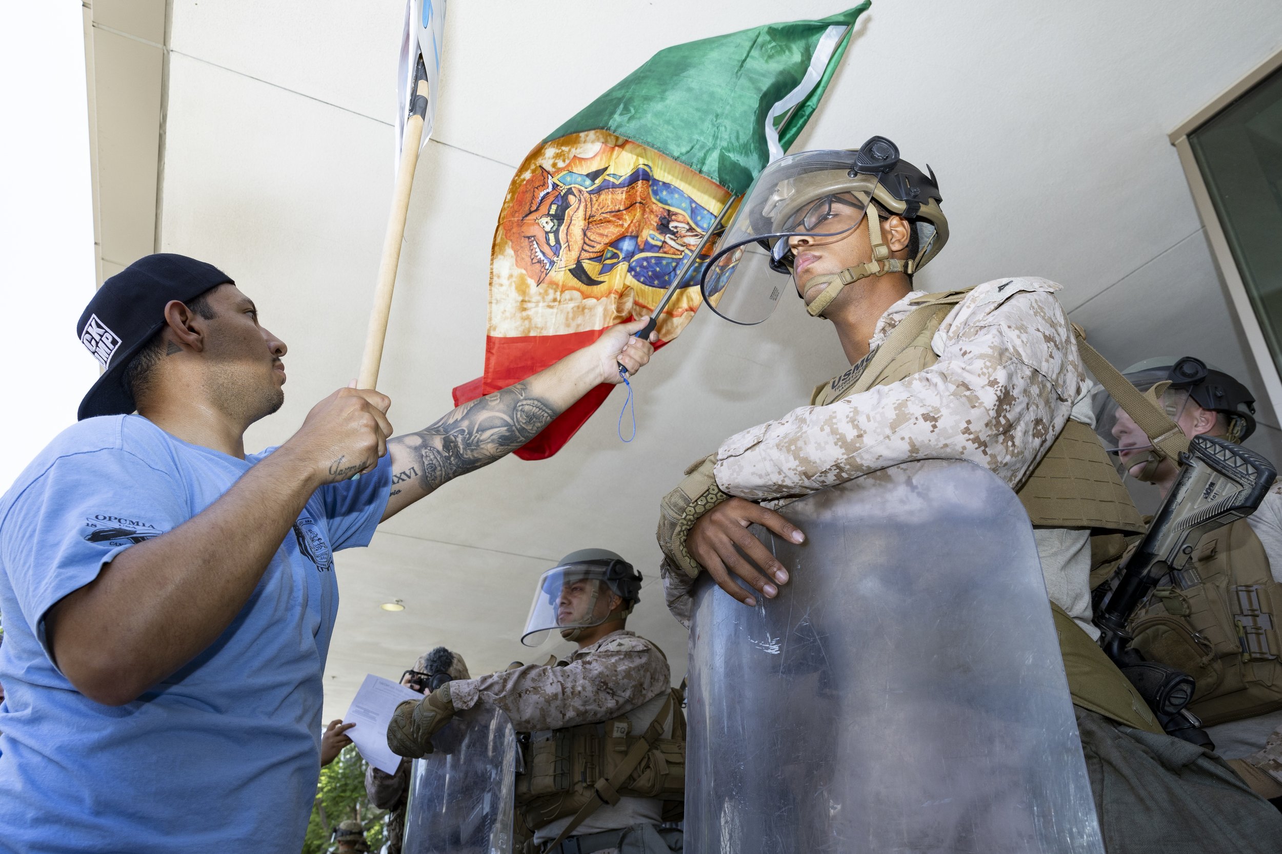 A protester waves a Mexican flag in front of Marines guarding the Federal Building in Los Angeles, Calif., on Friday, July 4, 2025. 50501 SOCAL organized a protest called End The Occupation, criticizing the Trump administration’s passing of the Big