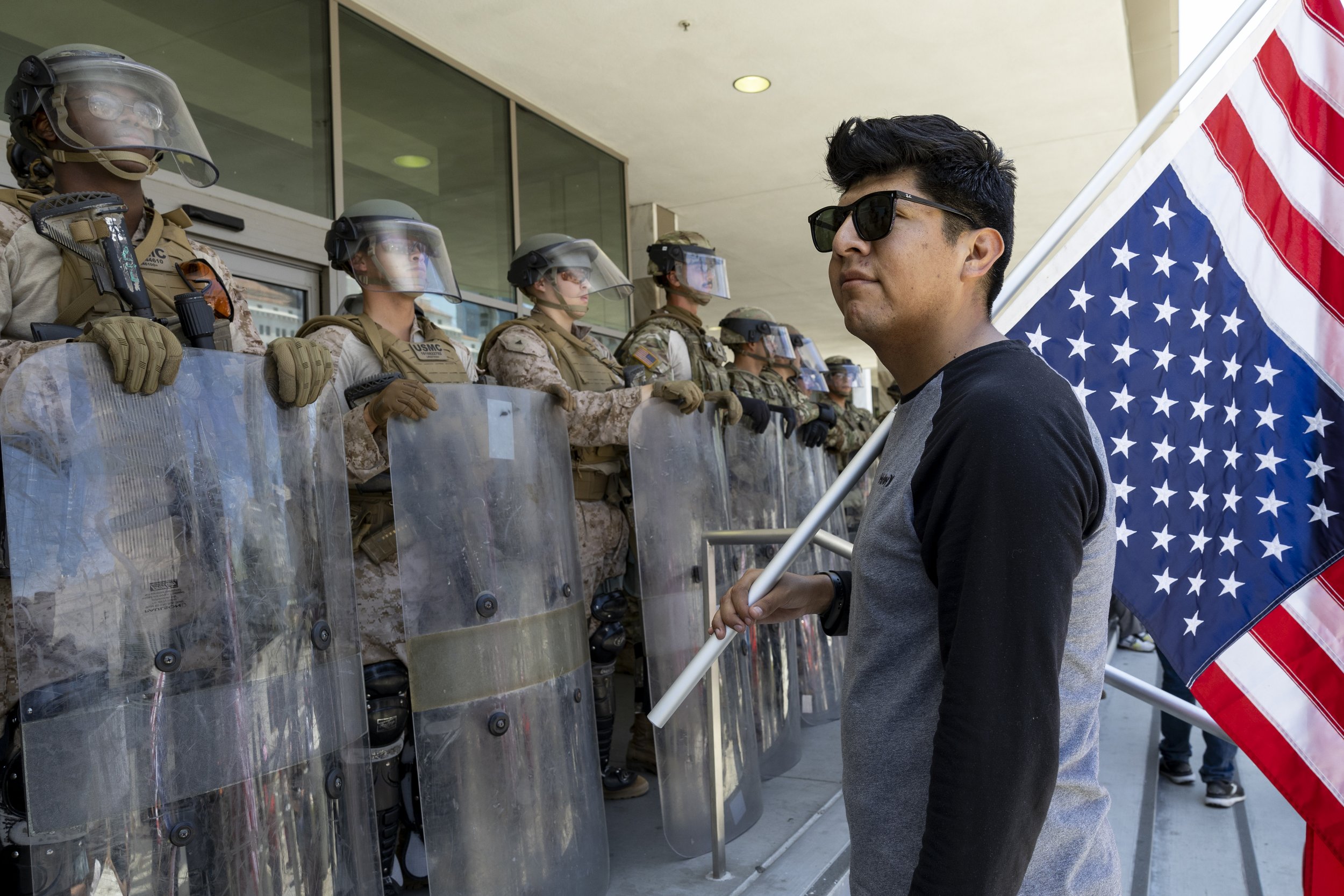 A protester holds an upside-down American flag in front of Marines guarding the Federal Building in Los Angeles, Calif., on Friday, July 4, 2025. 50501 SOCAL organized a protest called End The Occupation, criticizing the Trump administration’s passi