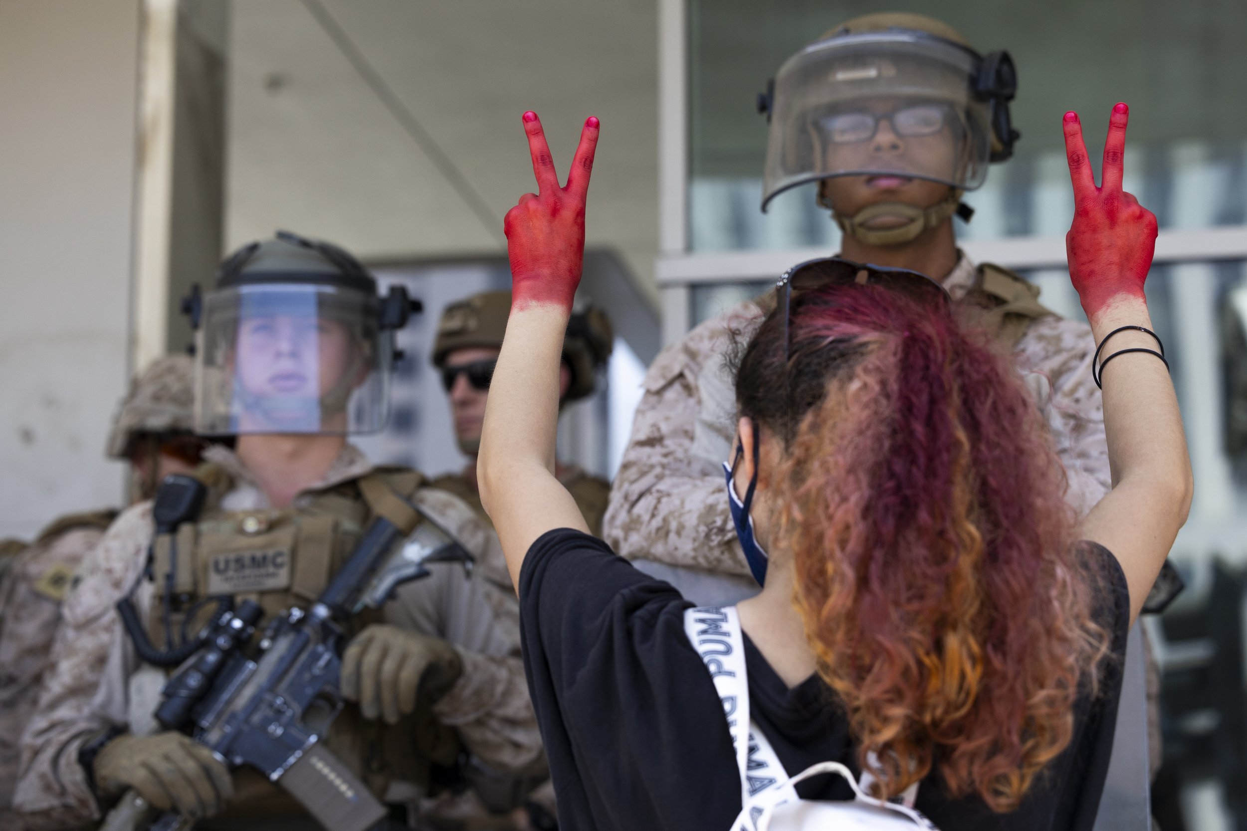 A protester holds her hands covered in red paint, making peace signs with her fingers to Marines guarding the Federal Building in Los Angeles, Calif., on Friday, July 4, 2025. 50501 SOCAL organized a protest called End The Occupation, criticizing th