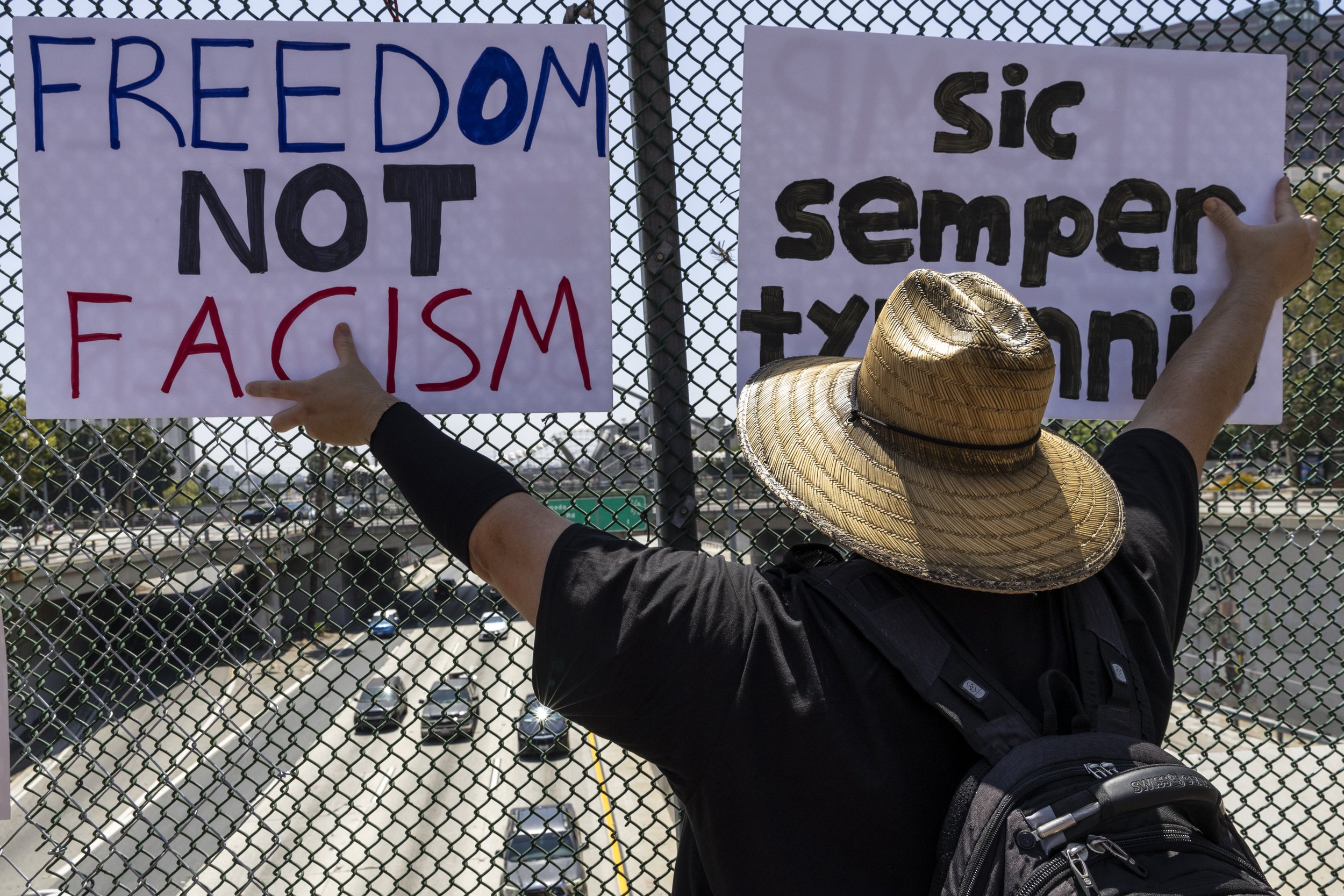 A protester holds up signs looking over Highway 101 during a protest in Los Angeles, Calif., on Friday, July 4, 2025. 50501 SOCAL organized a protest called End The Occupation, criticizing the Trump administration’s passing of the Big Beautiful Bill