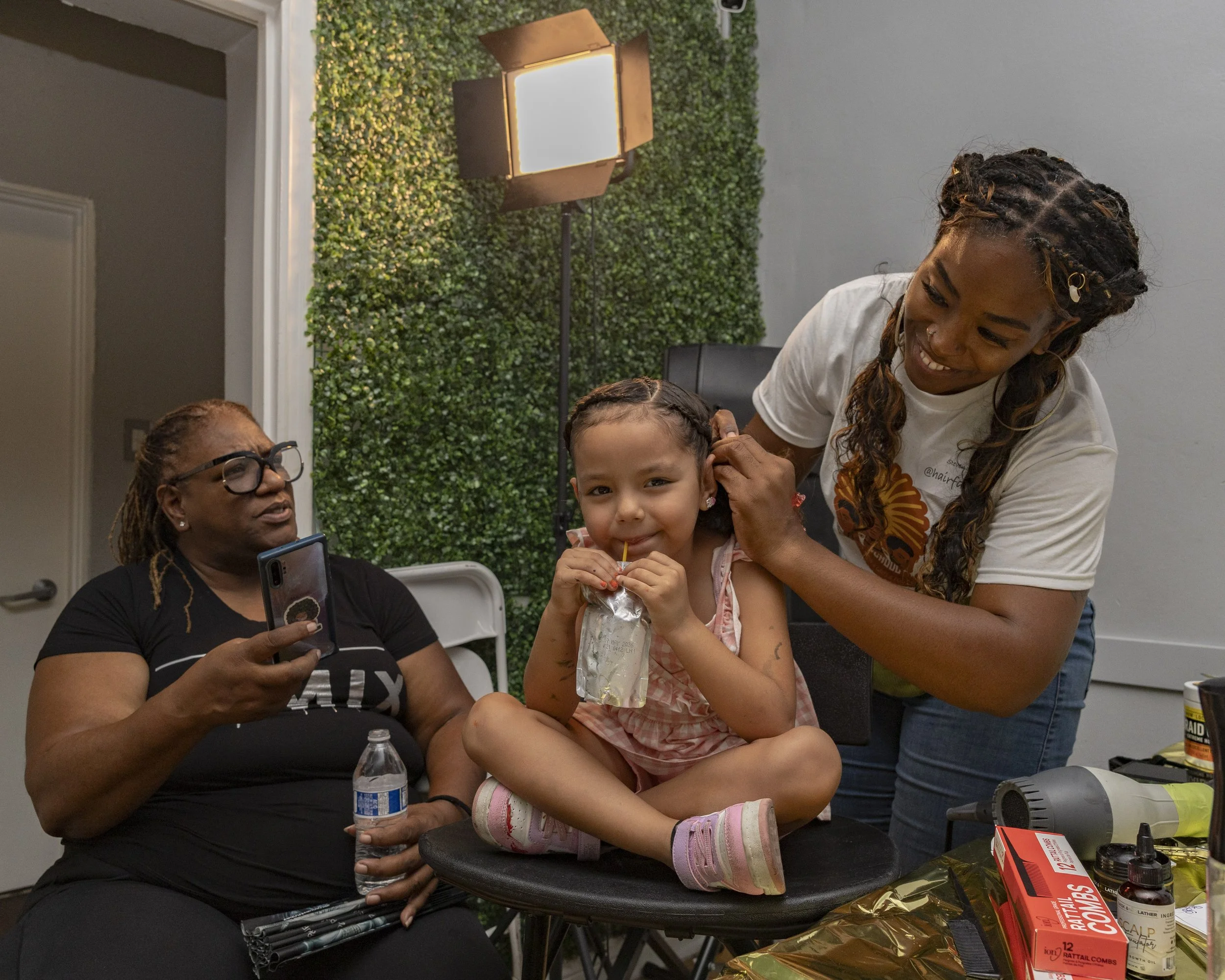 Stevenie Farmer (Right) braided hair at a Umoja Now mutual event at Event Space Inglewood in Inglewood, Calif., on Sunday, Aug 10, 2025, preparing children for school in a historically marginalized city. (Kayjel J. Mairena | The Corsair)