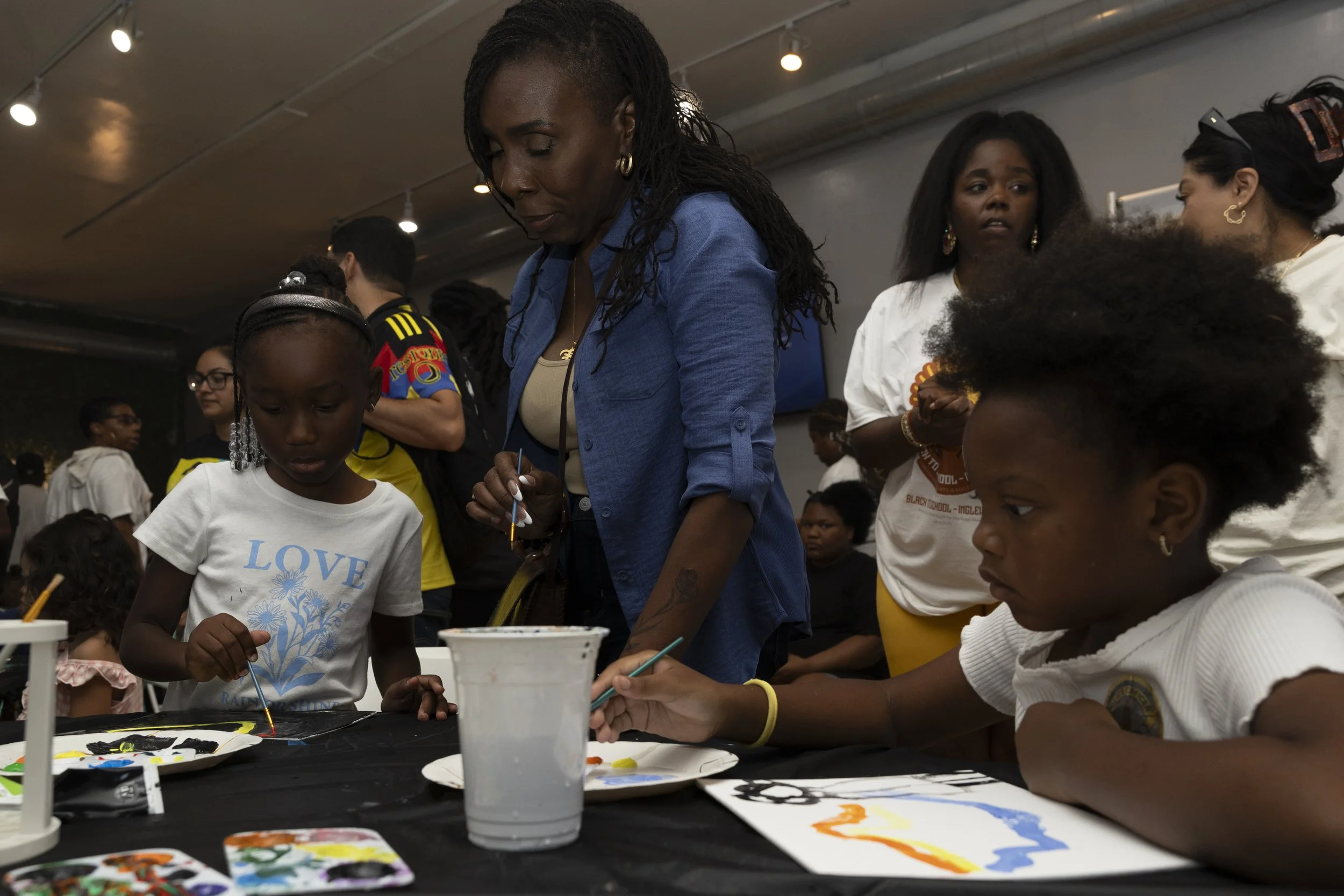 Nichelle Henderson (Center) watched her daughter paint at a Umoja Now mutual aid event inside Event Space Inglewood in Inglewood, Calif., on Sunday, Aug. 10, 2025, before presenting a certificate of recognition from the office of state Assemblymembe