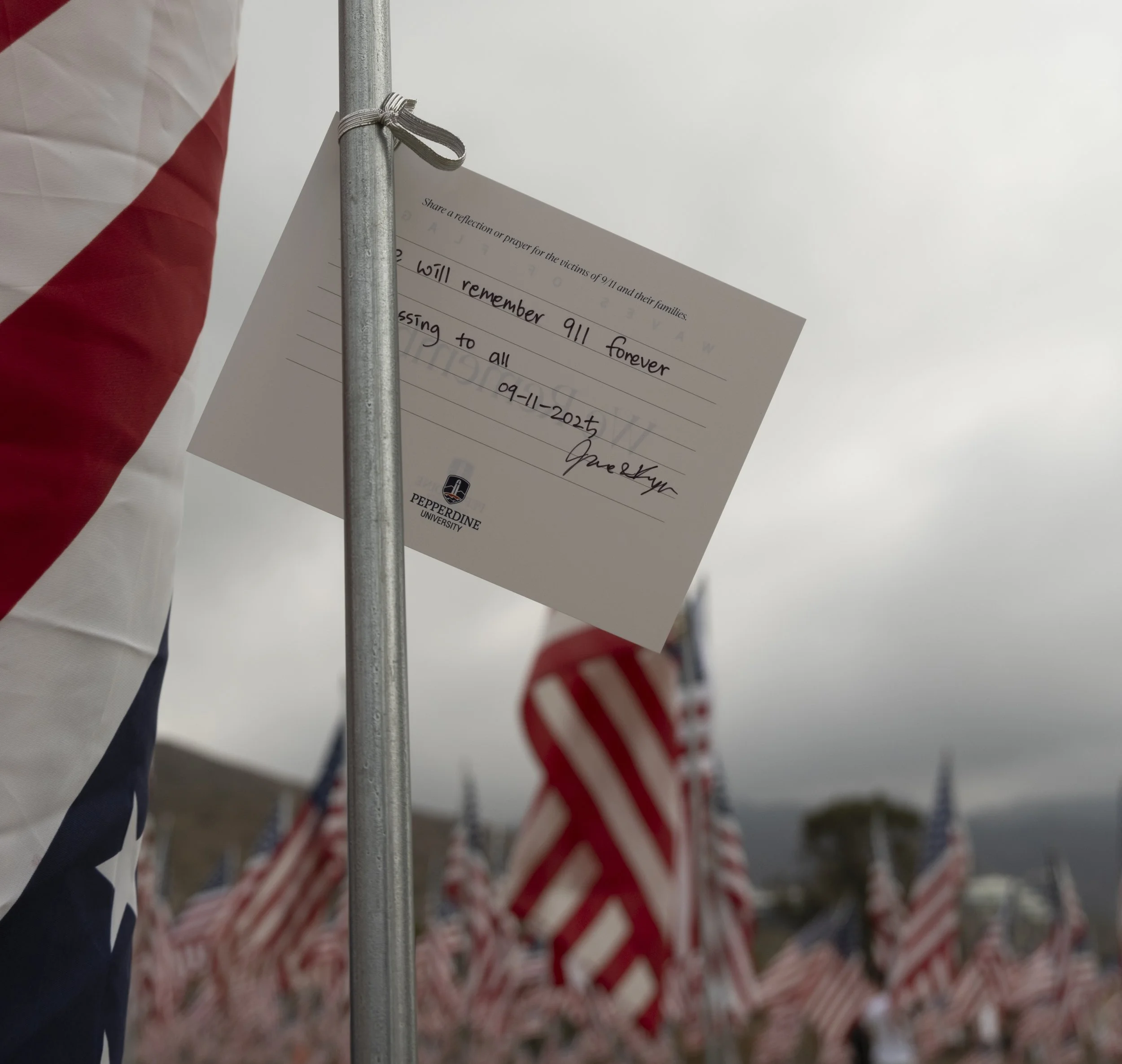 A card left by a visitor on one of the flags in “Waves of Flags”, the annual installation of nearly 3000 flags, one for each victim of 9/11, at Pepperdine University, Malibu, Calif. on Thursday, Sept 11, 2025. (Fai Fong | The Corsair)