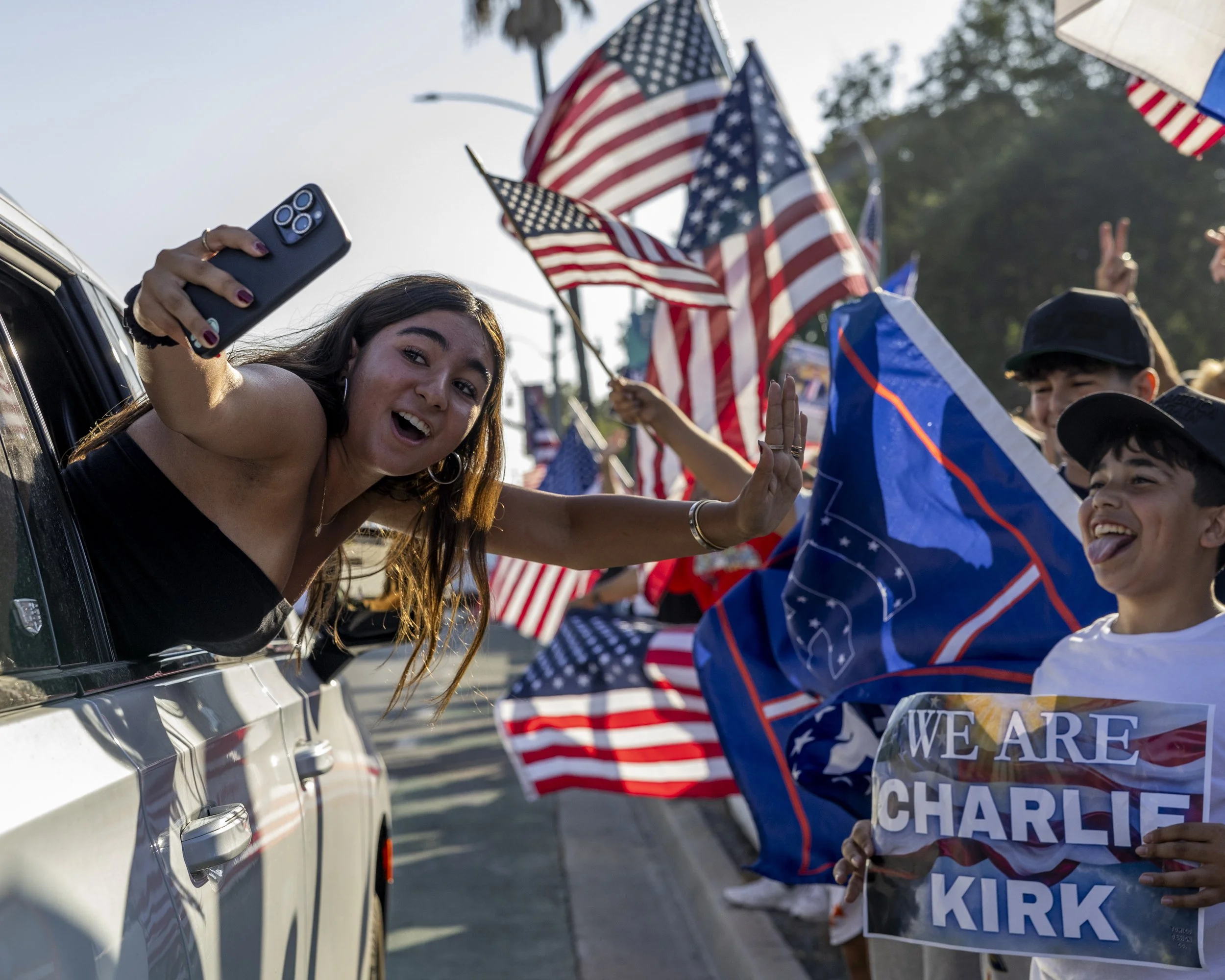 A girl hangs out the side of a car to take a photo of a boy holding a “We are Charlie Kirk” sign at a vigil for Charlie Kirk held by the Beverly Hills Freedom Rally, a rightwing activist group, on Sunday, Sept 14, 2025, in Beverly Hills, Calif.(Jake